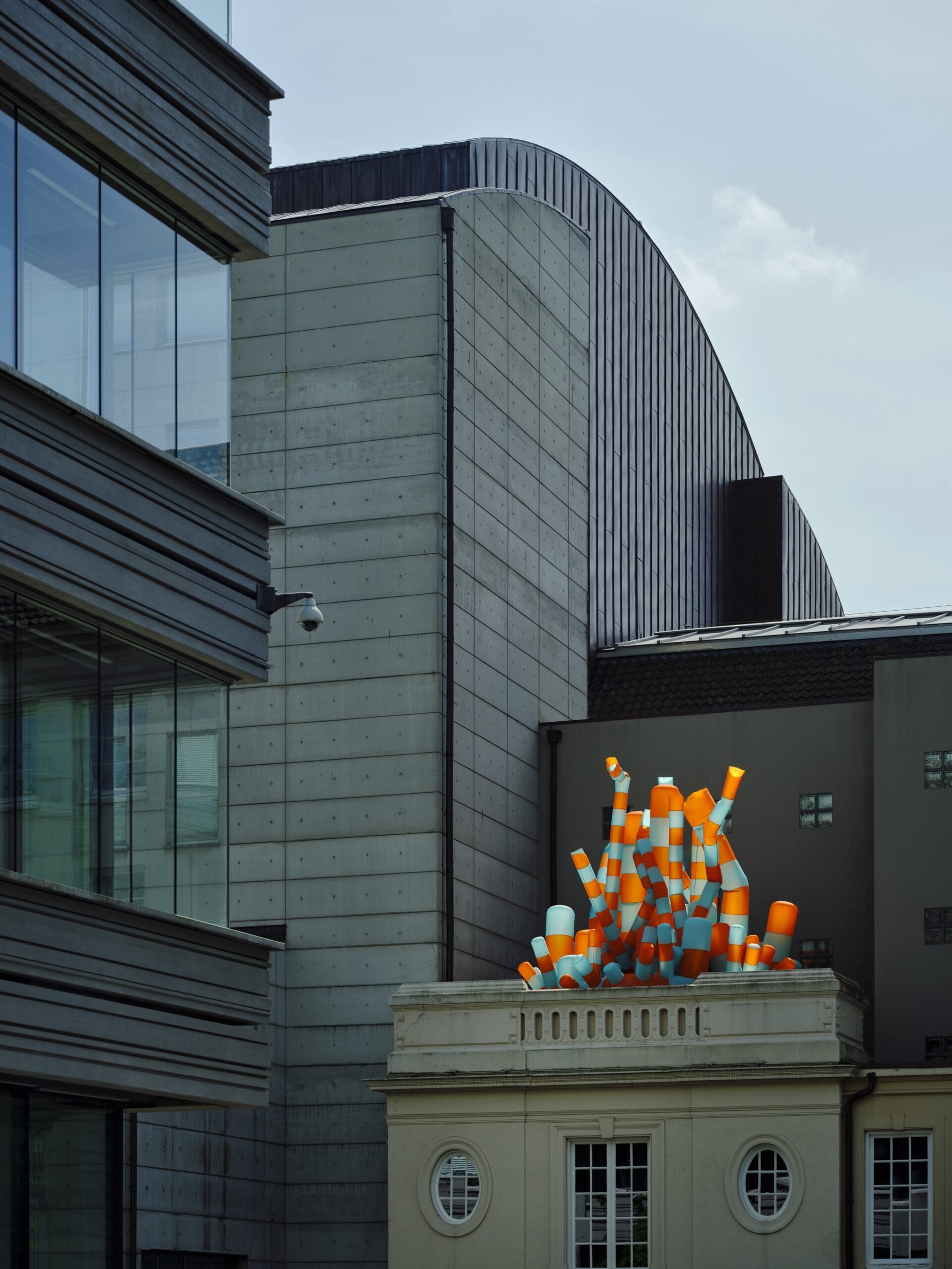 Een modern oranje en blauw gestreept kunstwerk op het dak van een klassiek gebouw, omringd door moderne architectuur