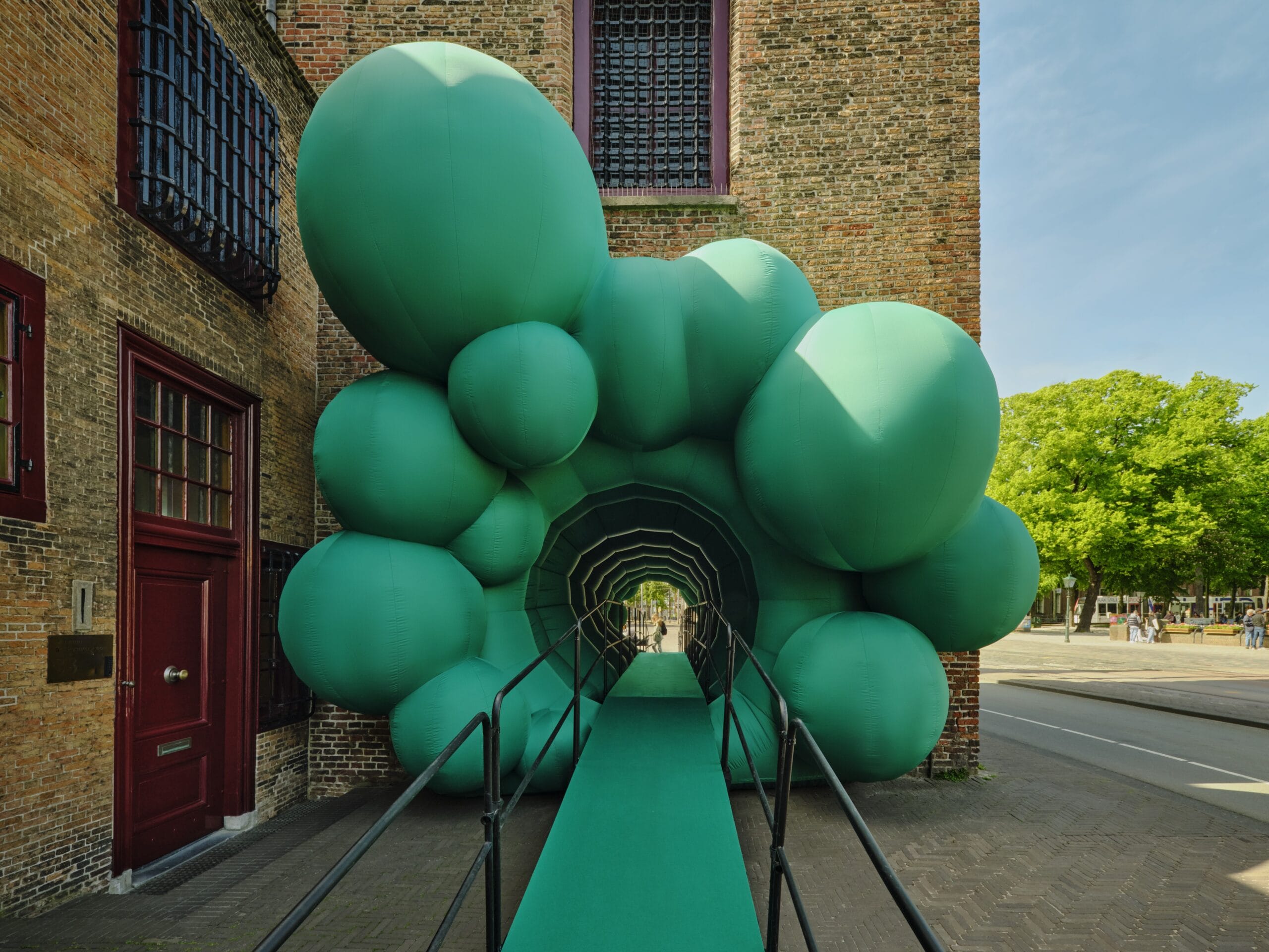 Een opblaasbare groene tunnel van bolvormige segmenten die de ingang van een historisch bakstenen gebouw vormt