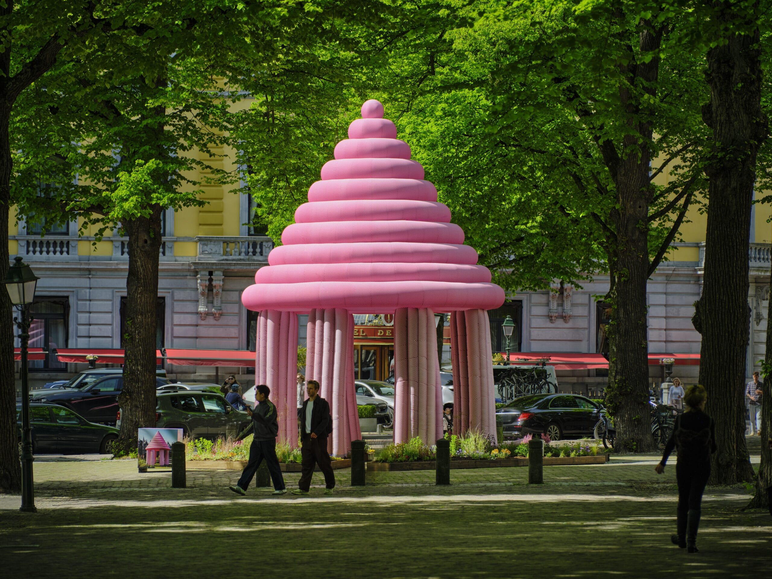Een groot roze opblaasbaar kunstwerk in de vorm van een paviljoen op een plein met bomen