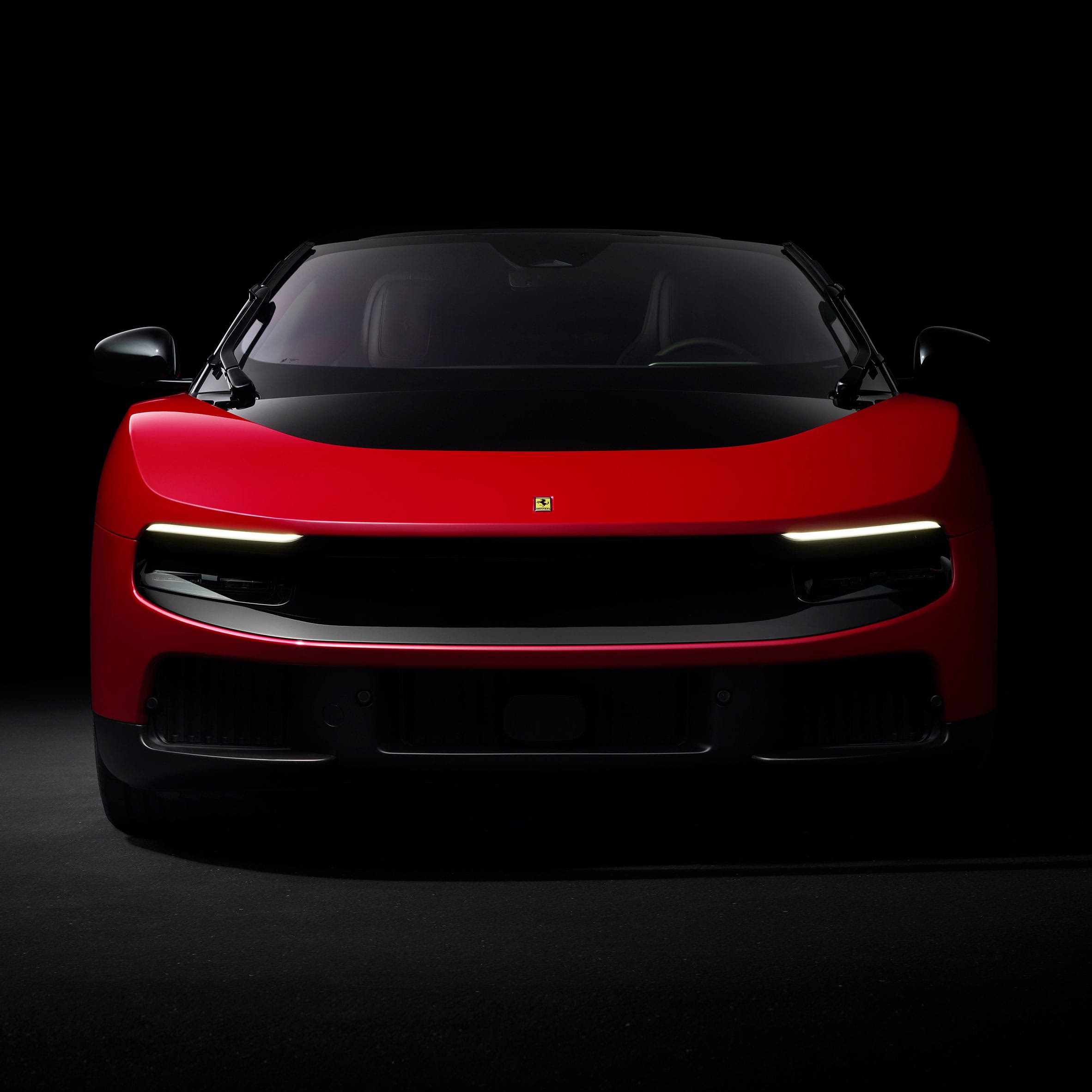 Vooraanzicht van een rode Ferrari Luce tegen een zwarte achtergrond met brandende dagrijverlichting