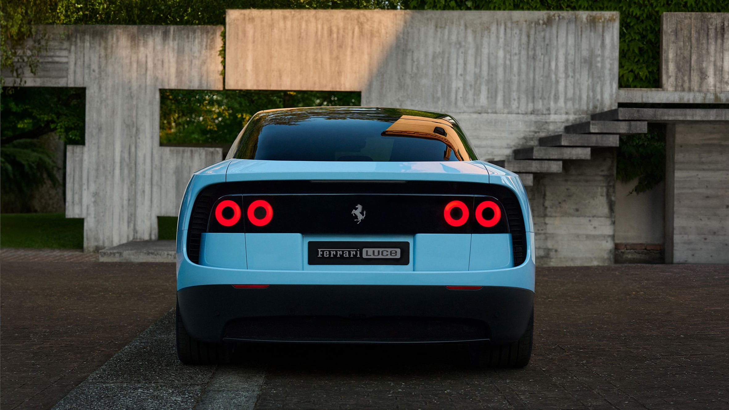 Achteraanzicht van een lichtblauwe Ferrari Luce met ronde rode achterlichten voor een betonnen architectonisch bouwwerk
