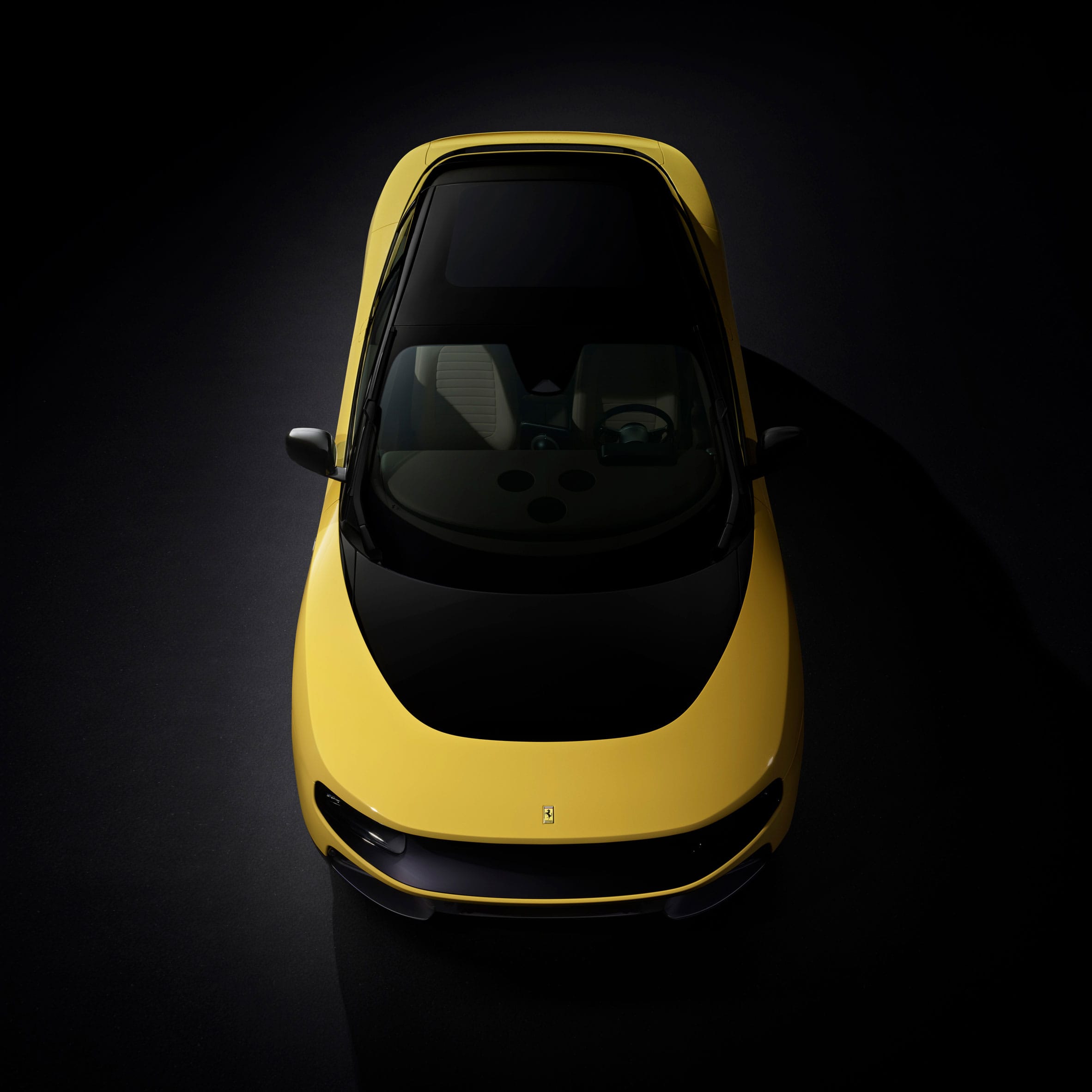 Bovenaanzicht van een gele Ferrari Luce met een zwart panoramisch dak tegen een donkere achtergrond