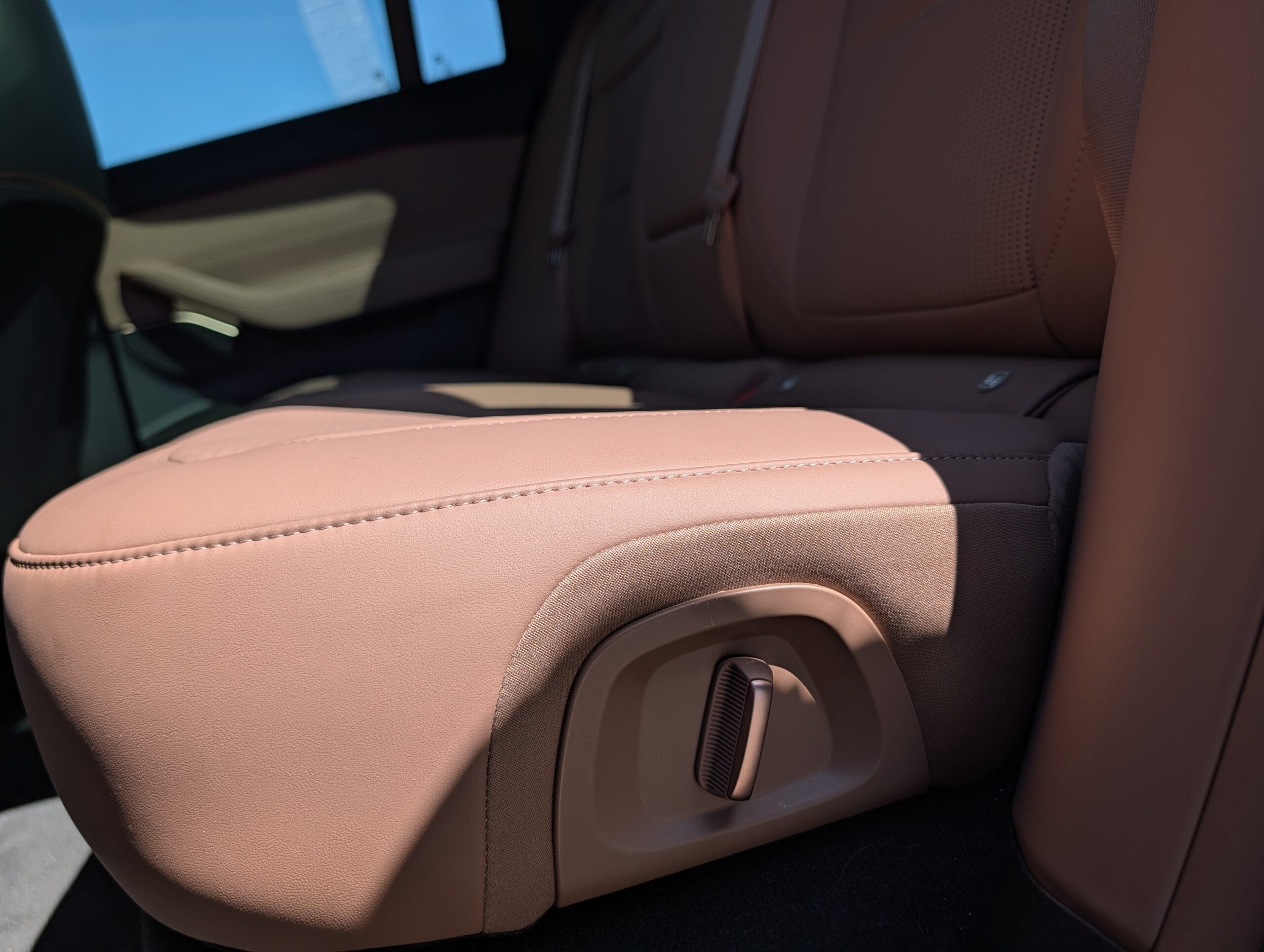 Bedieningsknop aan de zijkant van een bruin lederen achterbank in een auto voor het elektrisch inklappen van de stoelen
