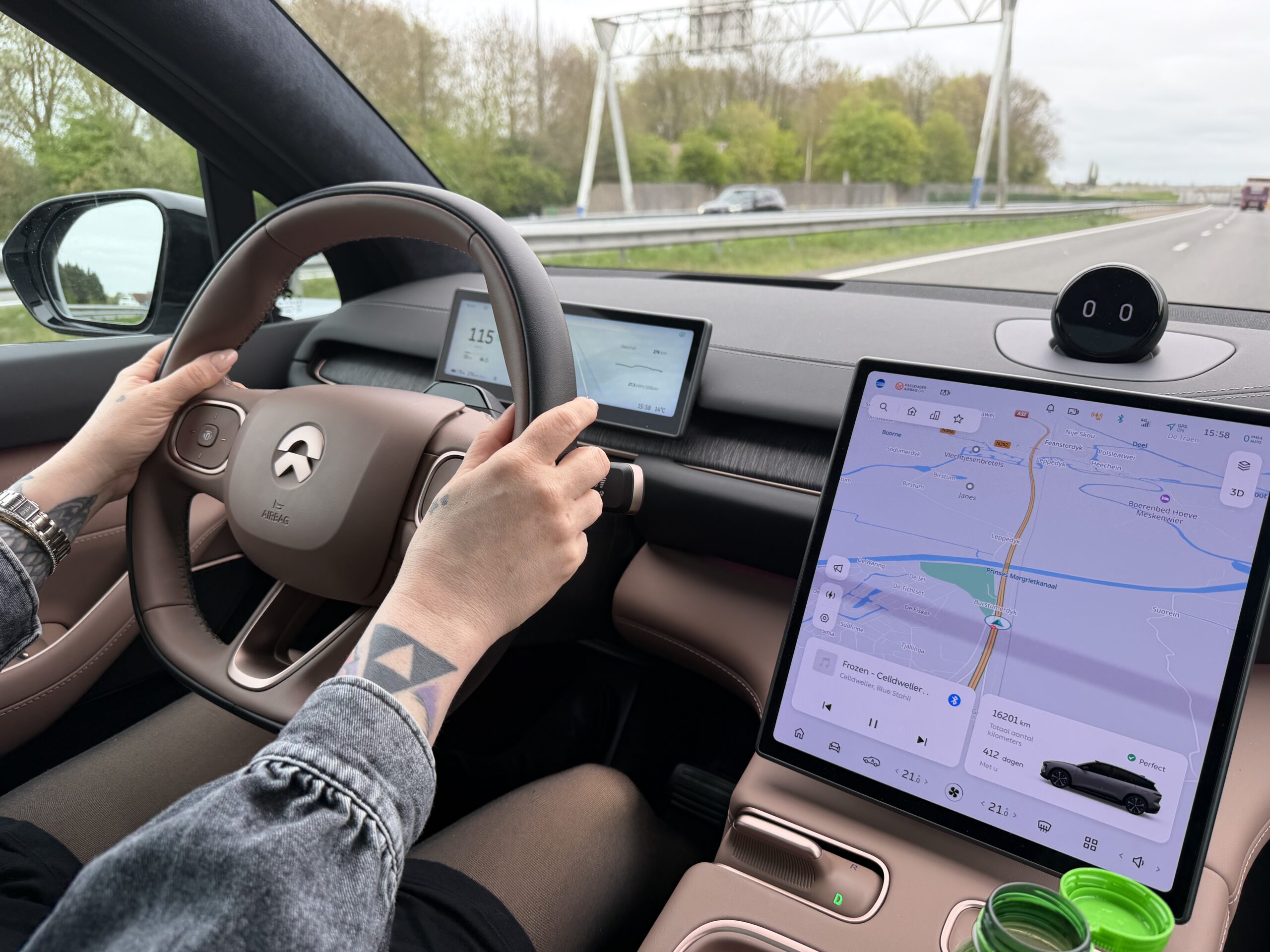 Bestuurder met getatoeëerde armen aan het stuur van een NIO op de snelweg, met navigatie op het centrale display