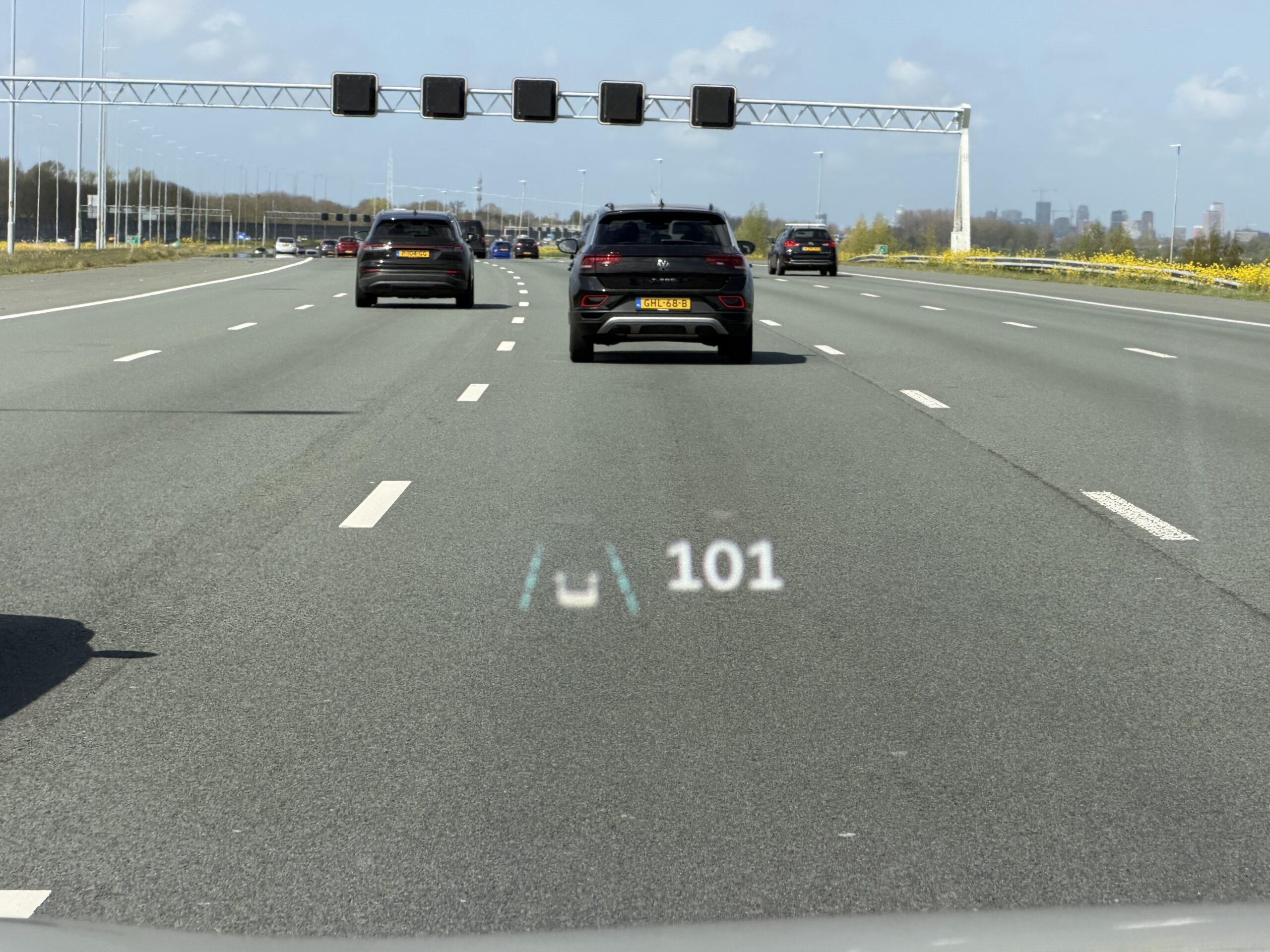Zicht vanuit een auto op een snelweg met een head-up display dat een snelheid van 101 km/u en rijstrookassistentie toont