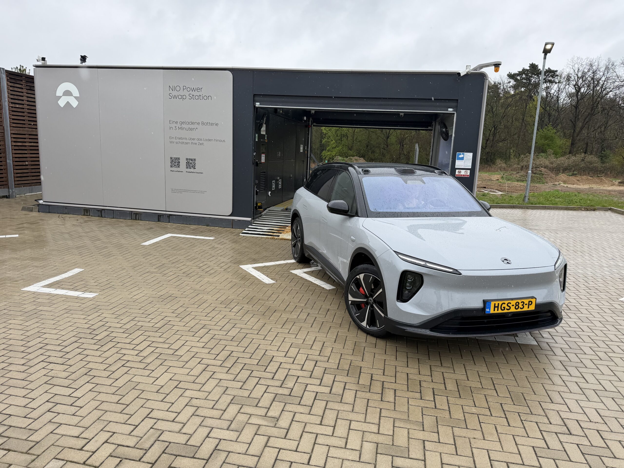 Een lichtgrijze NIO elektrische auto staat geparkeerd voor een NIO Power Swap Station voor het automatisch wisselen van accu's