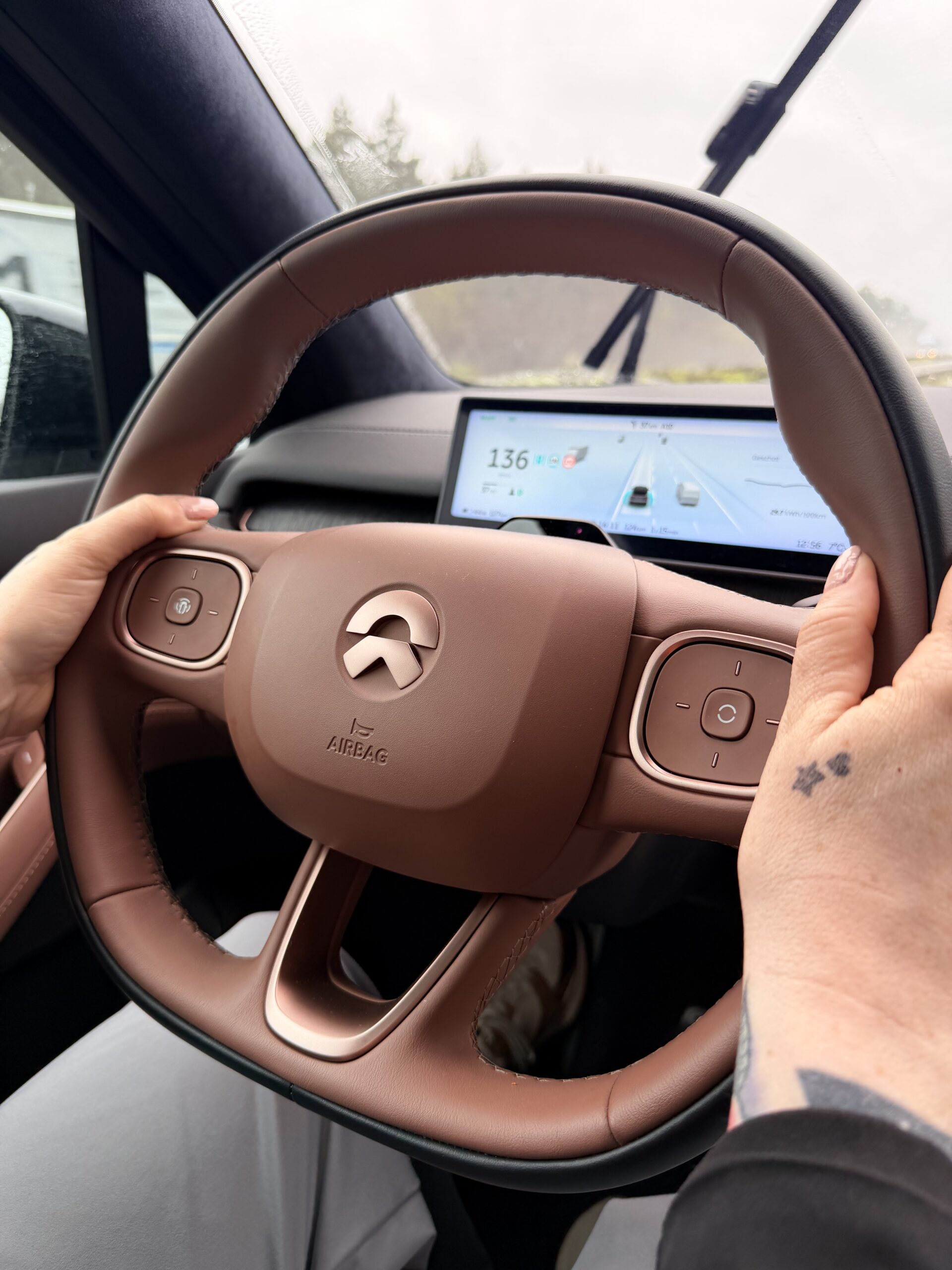Zicht van de bestuurder op het bruin lederen stuur van een NIO met het digitale dashboard op de achtergrond