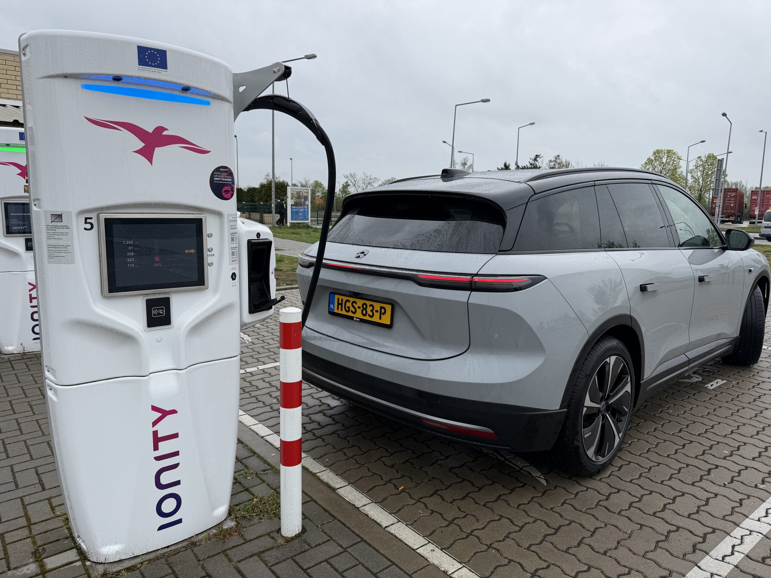 Een grijze elektrische auto aangesloten op een wit Ionity-snellaadstation op een parkeerplaats