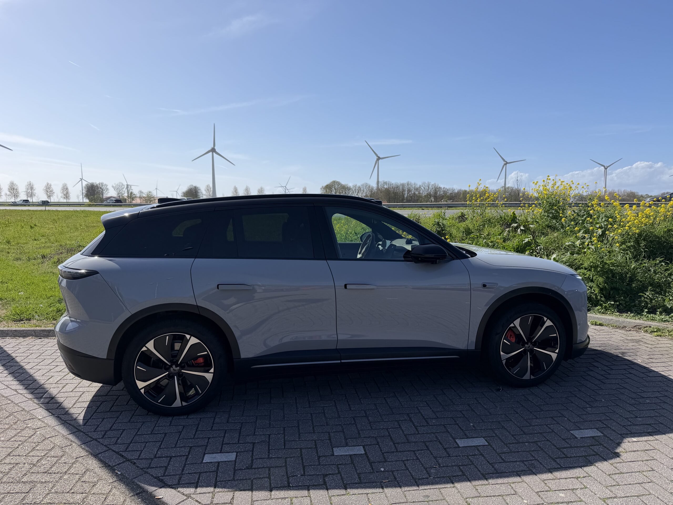Zijaanzicht van een grijze elektrische SUV geparkeerd op een klinkerweg met windmolens op de achtergrond