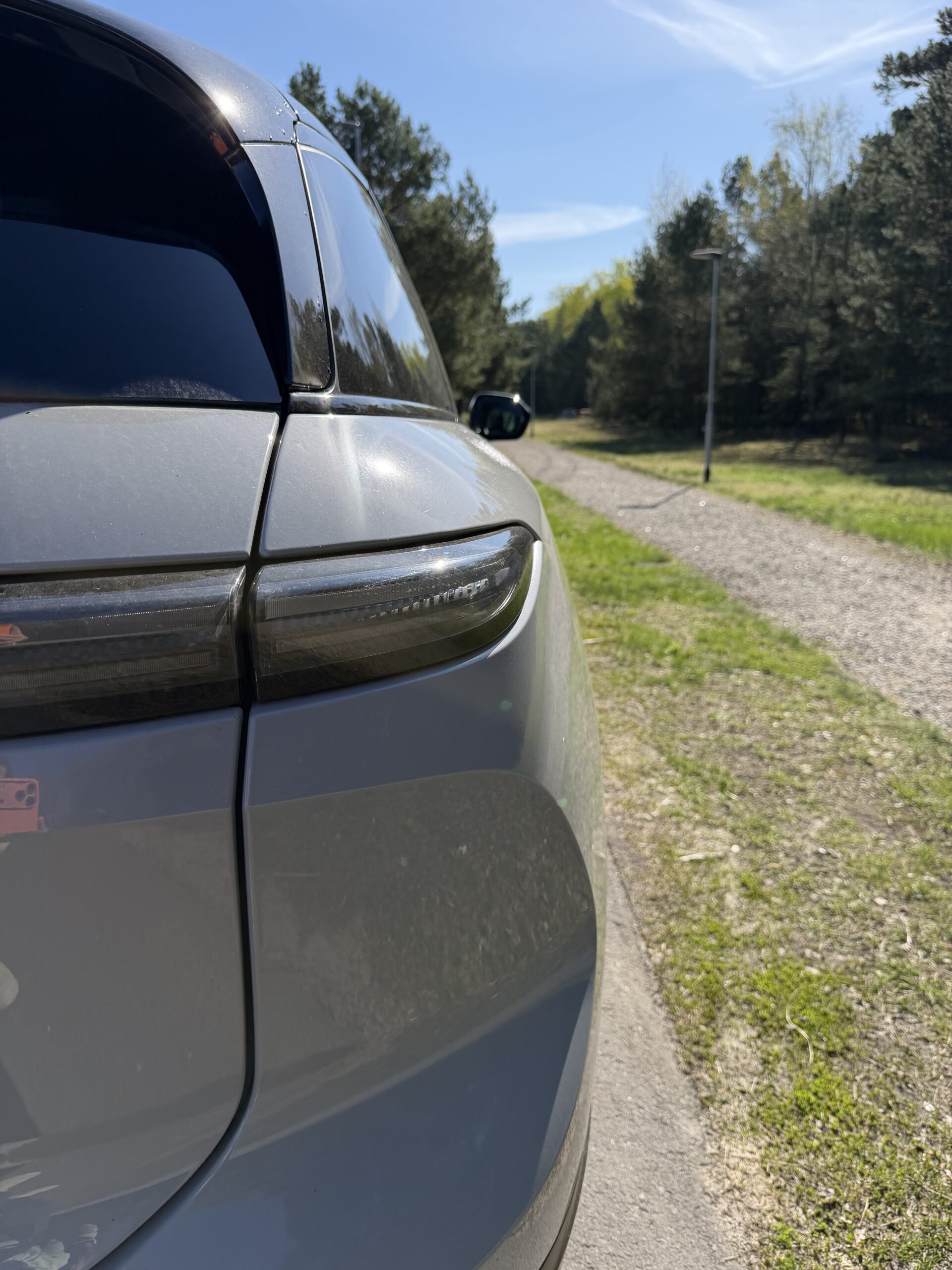 Close-up van het achterlicht en de zijkant van een grijze auto, geparkeerd langs een onverhard pad in een bosrijke omgeving