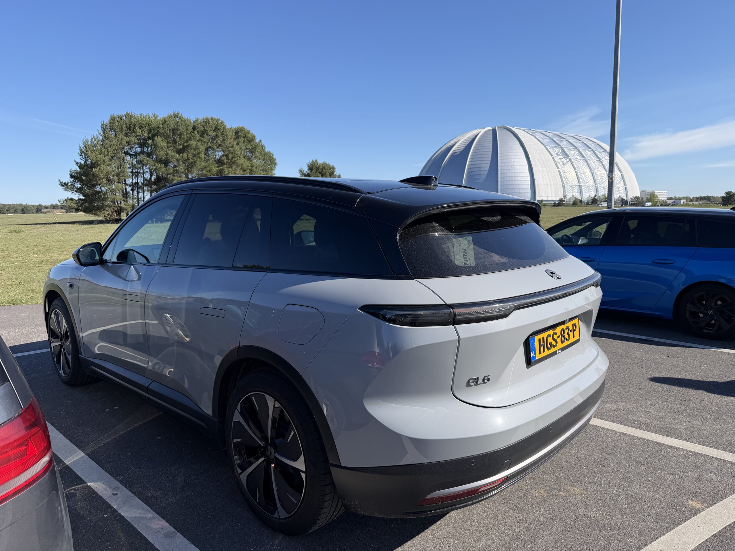Grijze NIO EL6 geparkeerd op een parkeerplaats met een grote witte koepel op de achtergrond