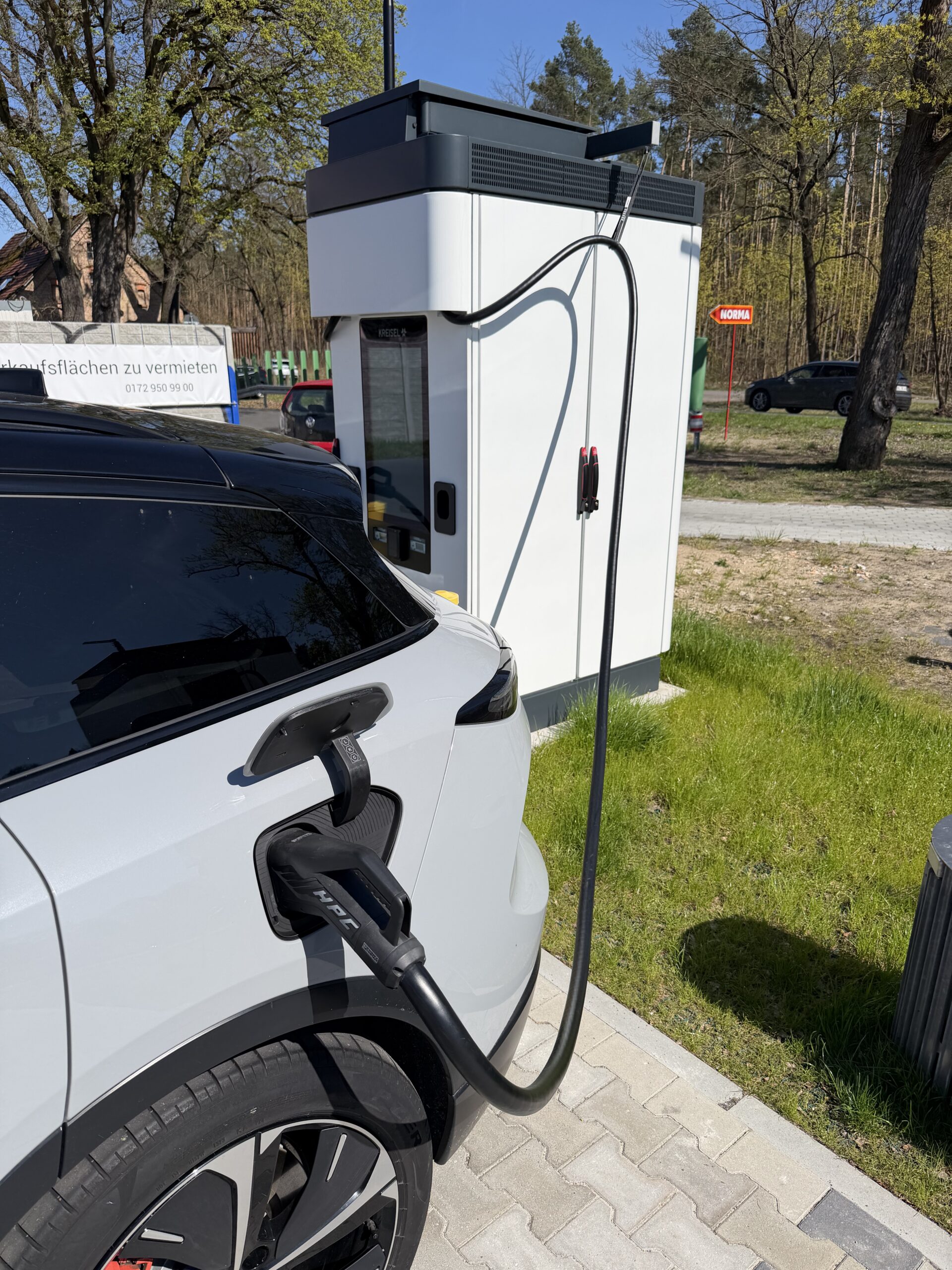 Een witte elektrische auto aangesloten op een snellaadstation bij een parkeerplaats