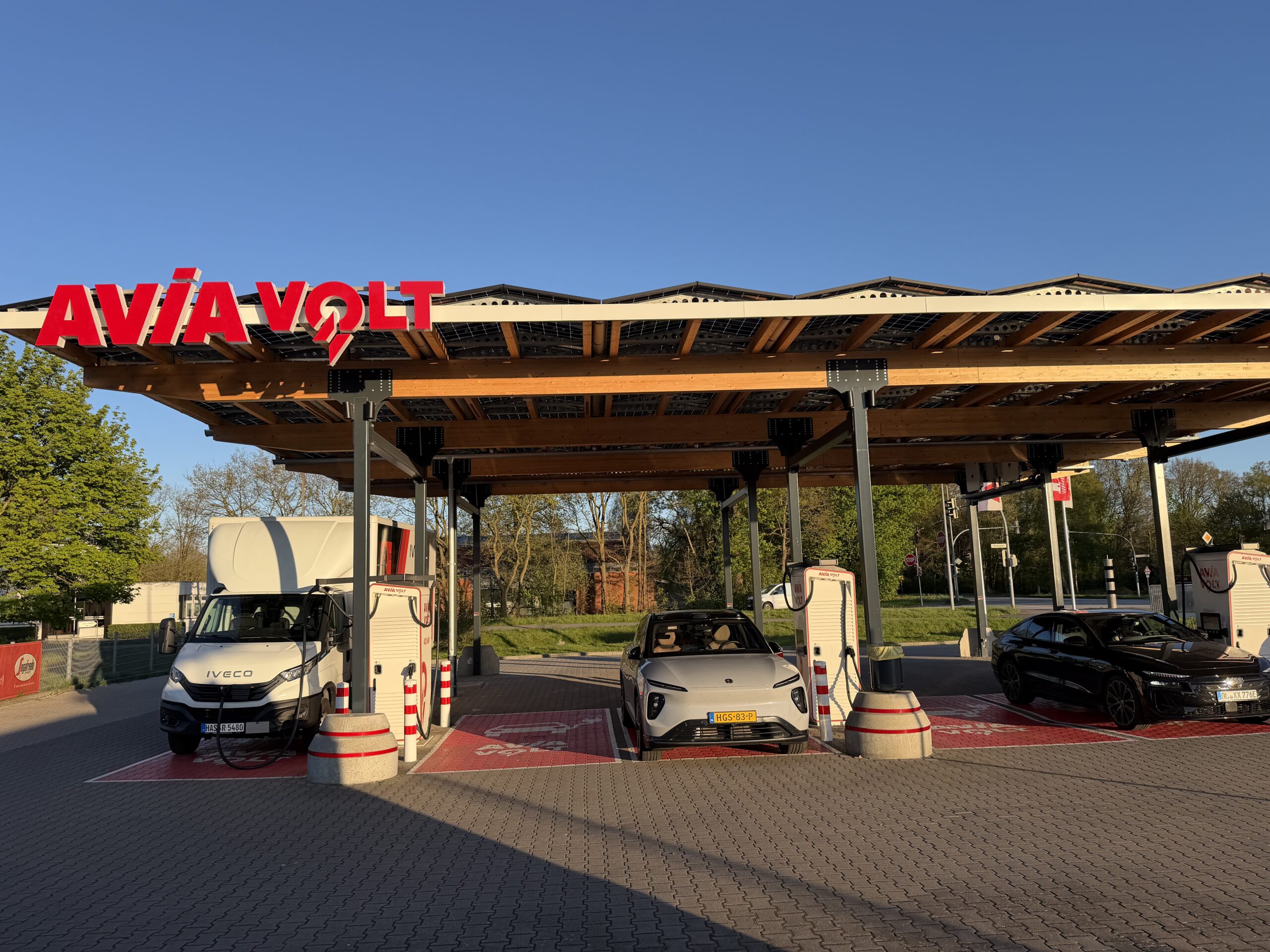 Elektrische auto's en een bestelwagen bij een Avia Volt snellaadstation onder een overkapping met zonnepanelen