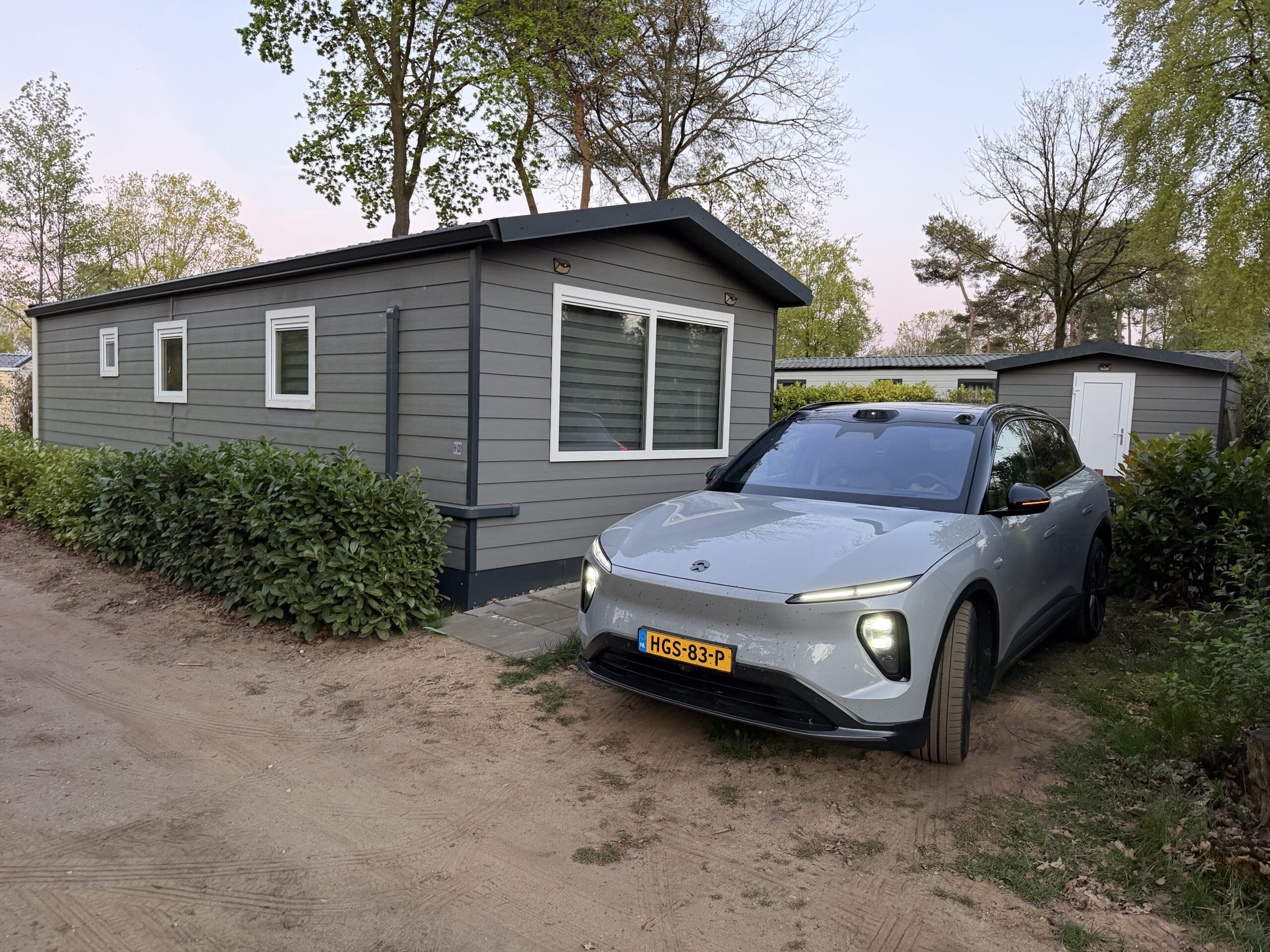 Een grijze elektrische NIO SUV geparkeerd voor een modern grijs chalet op een vakantiepark
