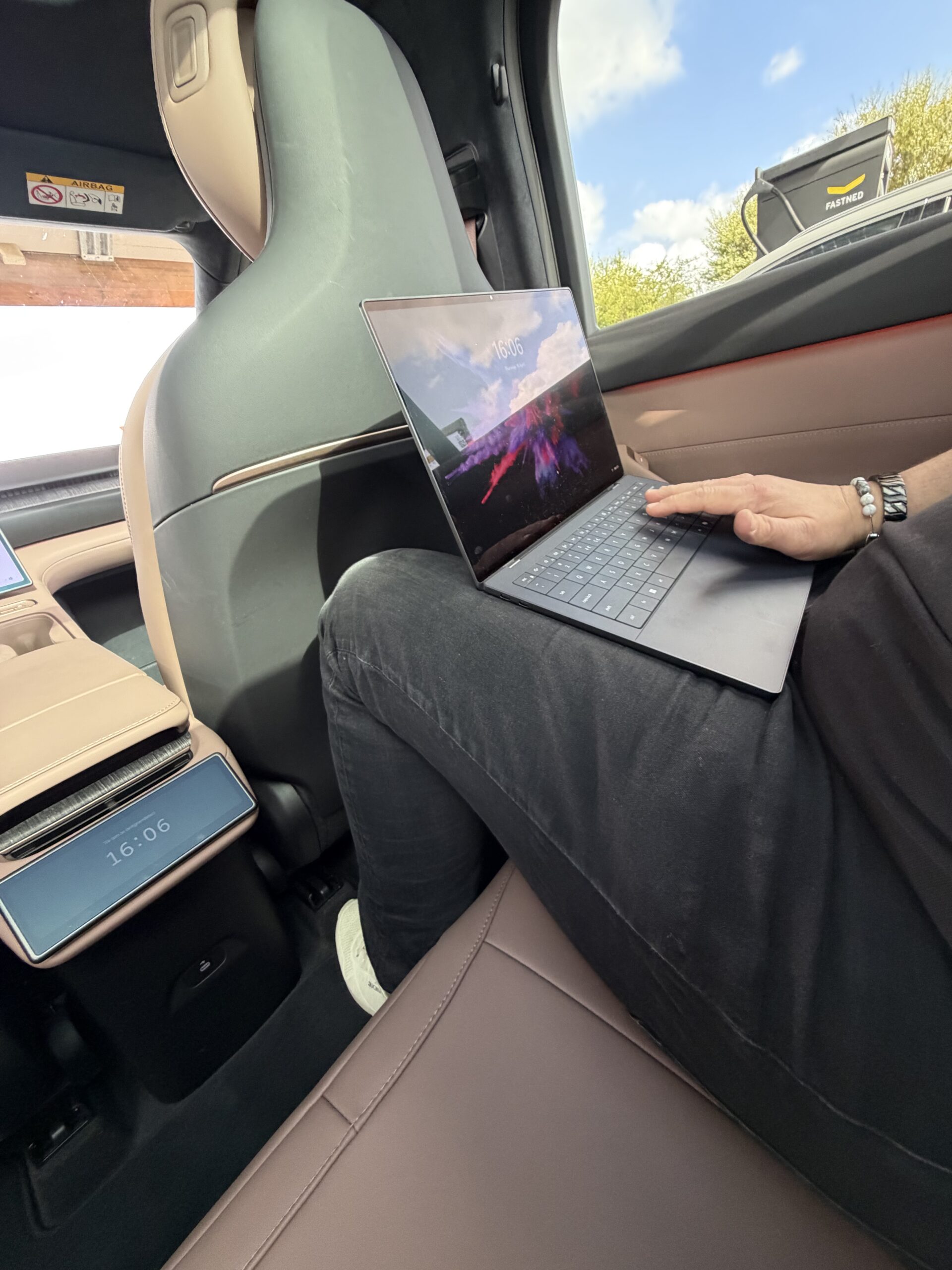 Een persoon werkt op een laptop op de achterbank van een auto terwijl deze oplaadt bij een Fastned-station