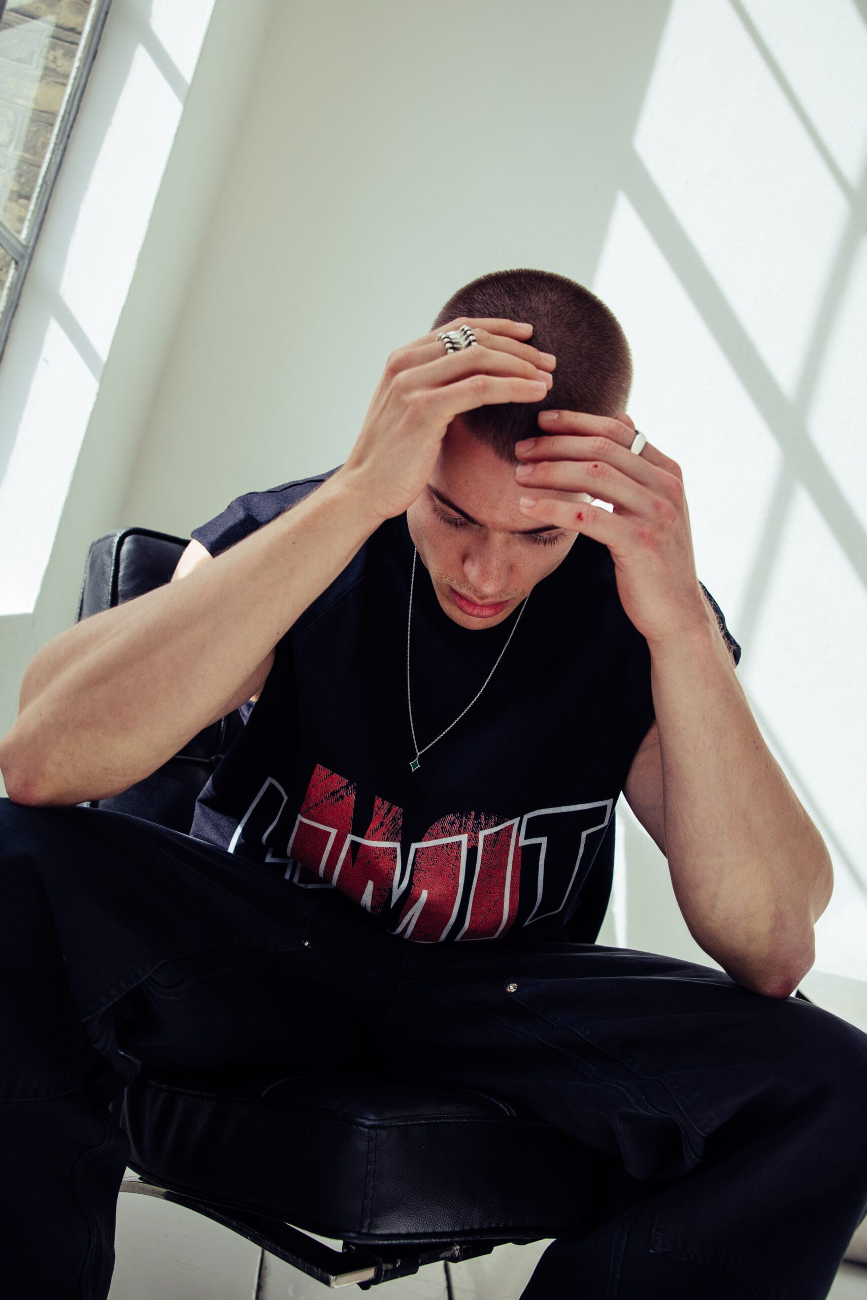 Zittende man met gemillimeterd haar houdt zijn hoofd vast en draagt een zwart mouwloos shirt met de tekst LIMIT