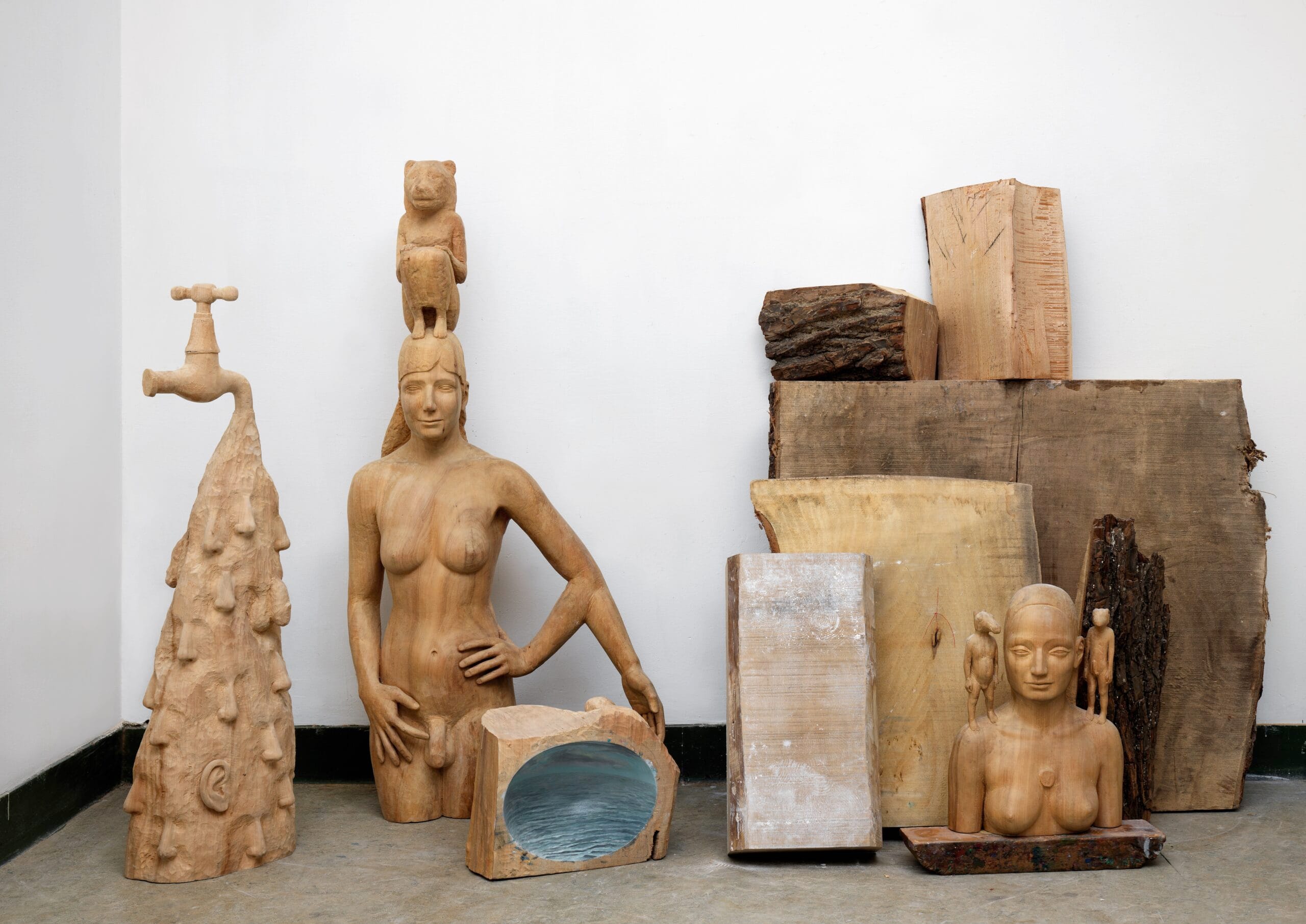 Houten sculpturen van menselijke figuren en abstracte vormen tegen een witte muur in het atelier van kunstenaar Femmy Otten 