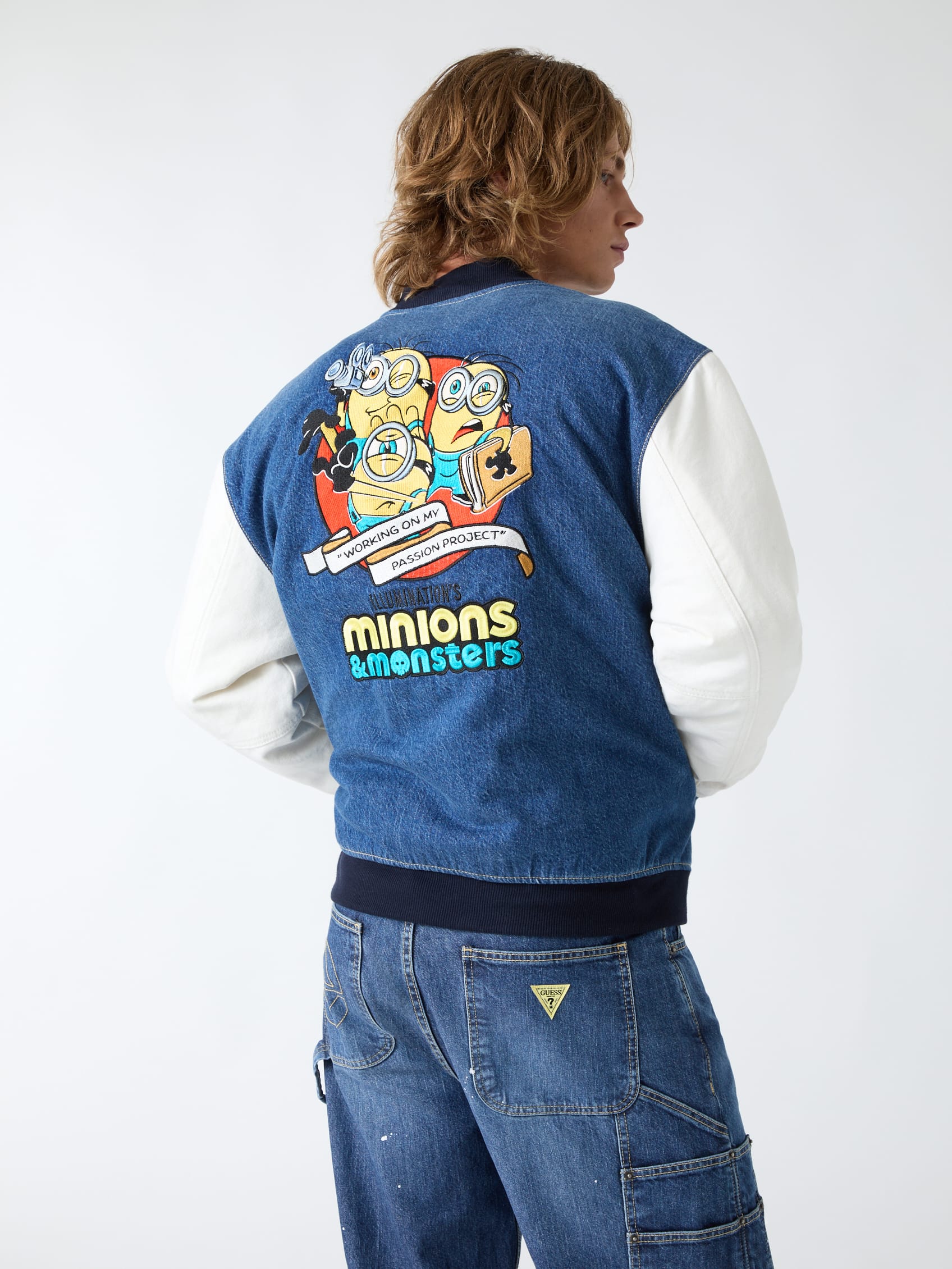 Achterkant van een denim varsity jack van modemerk Guess met Minions & Monsters-opdruk en witte mouwen