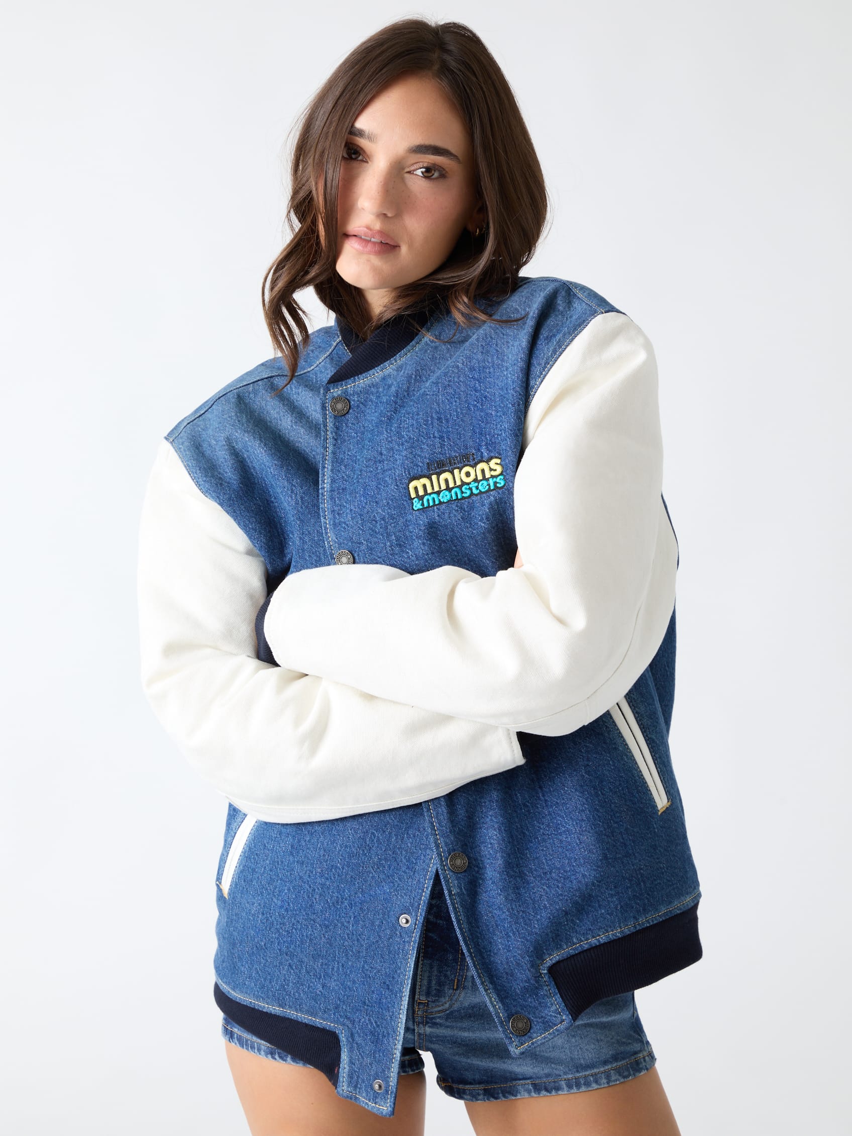 Vrouw in een denim varsity-jack van Guess met witte mouwen en het logo Minions & Monsters op de borst