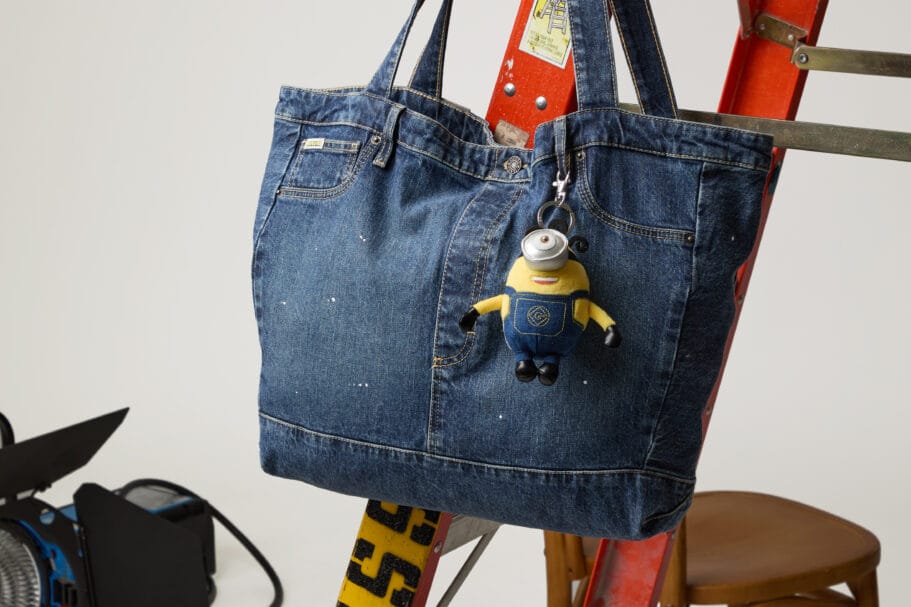 Blauwe denim shopper van Guess met een Minion-sleutelhanger, hangend aan een rode ladder in een fotostudio