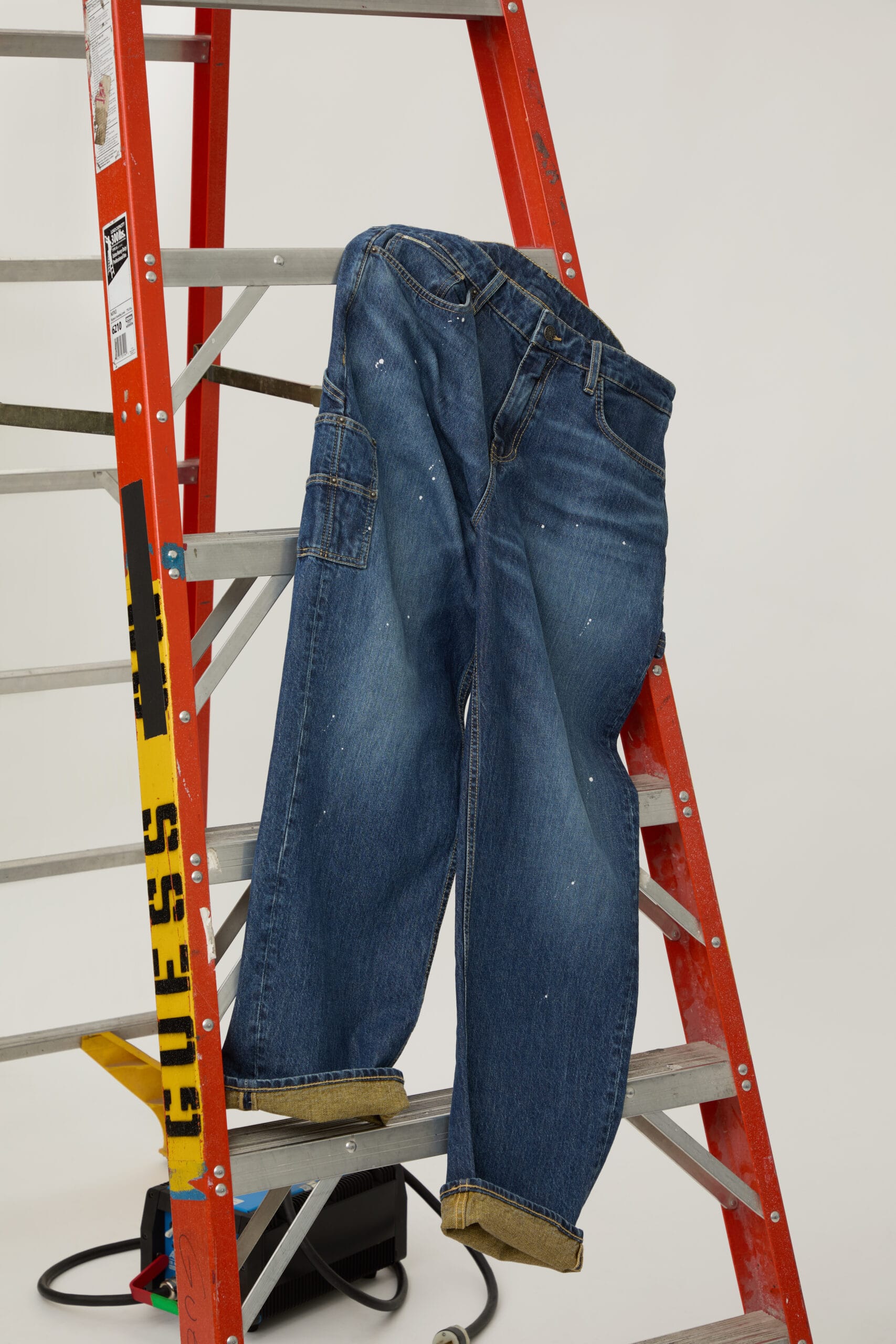 Donkerblauwe spijkerbroek van Guess met witte verfspatten over een oranje ladder gehangen