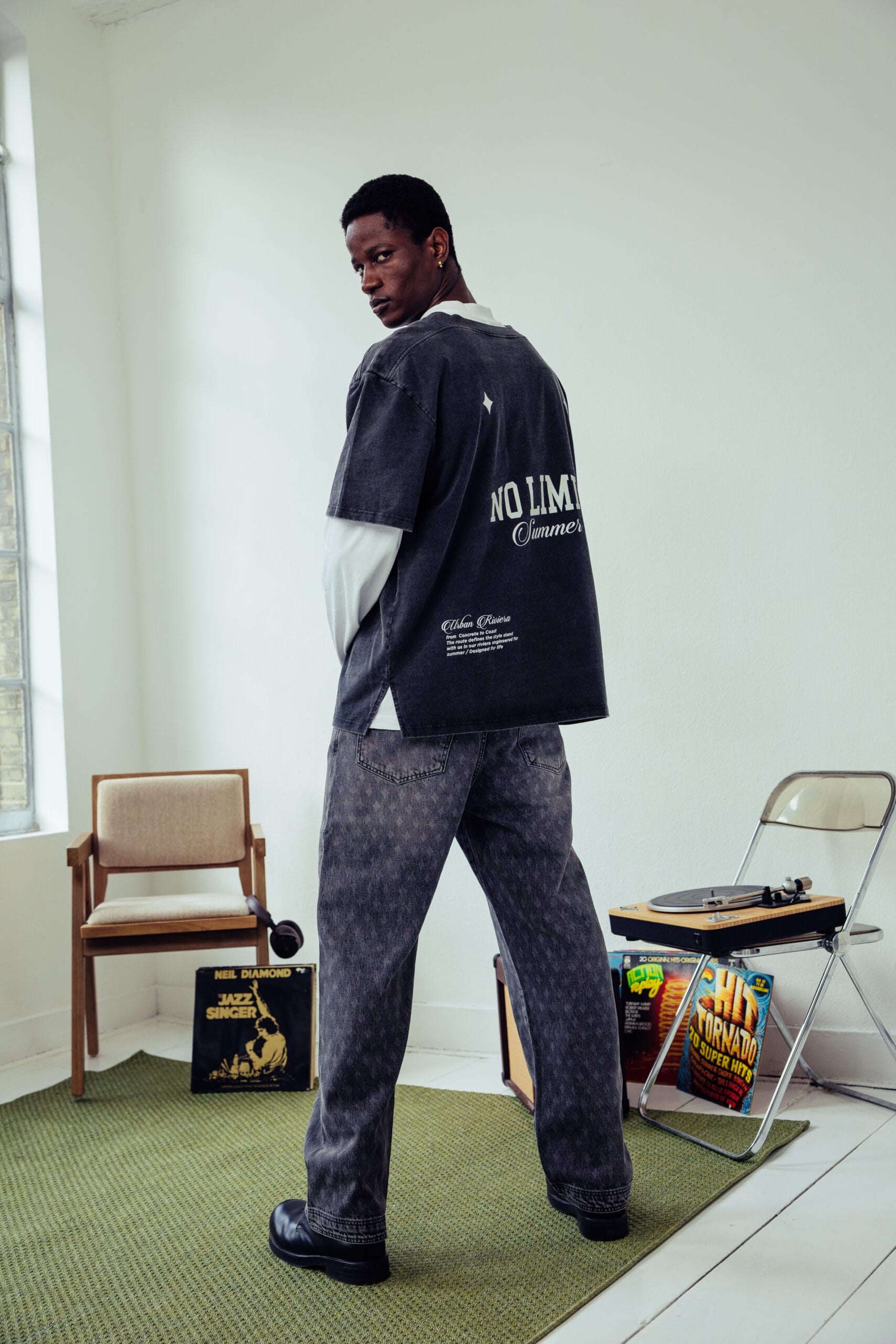 Man in een donkergrijs T-shirt met de tekst No Limit Summer op de rug en een wijde grijze jeans