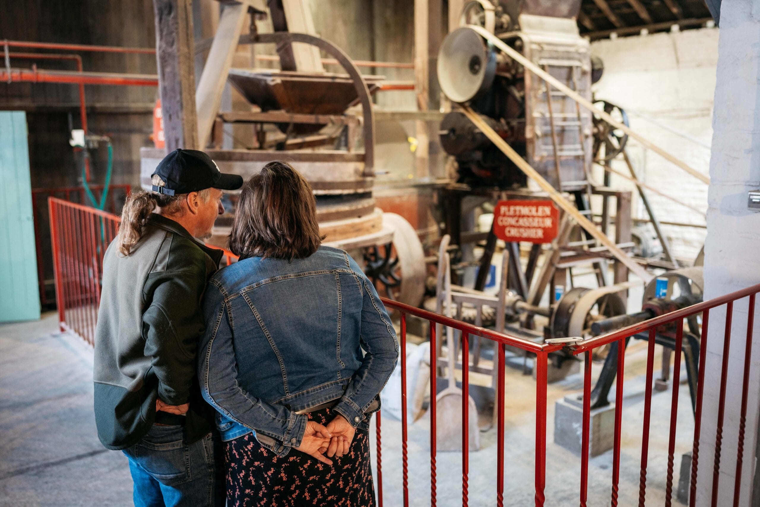 Twee bezoekers bekijken een historische pletmolen in een industriële omgeving