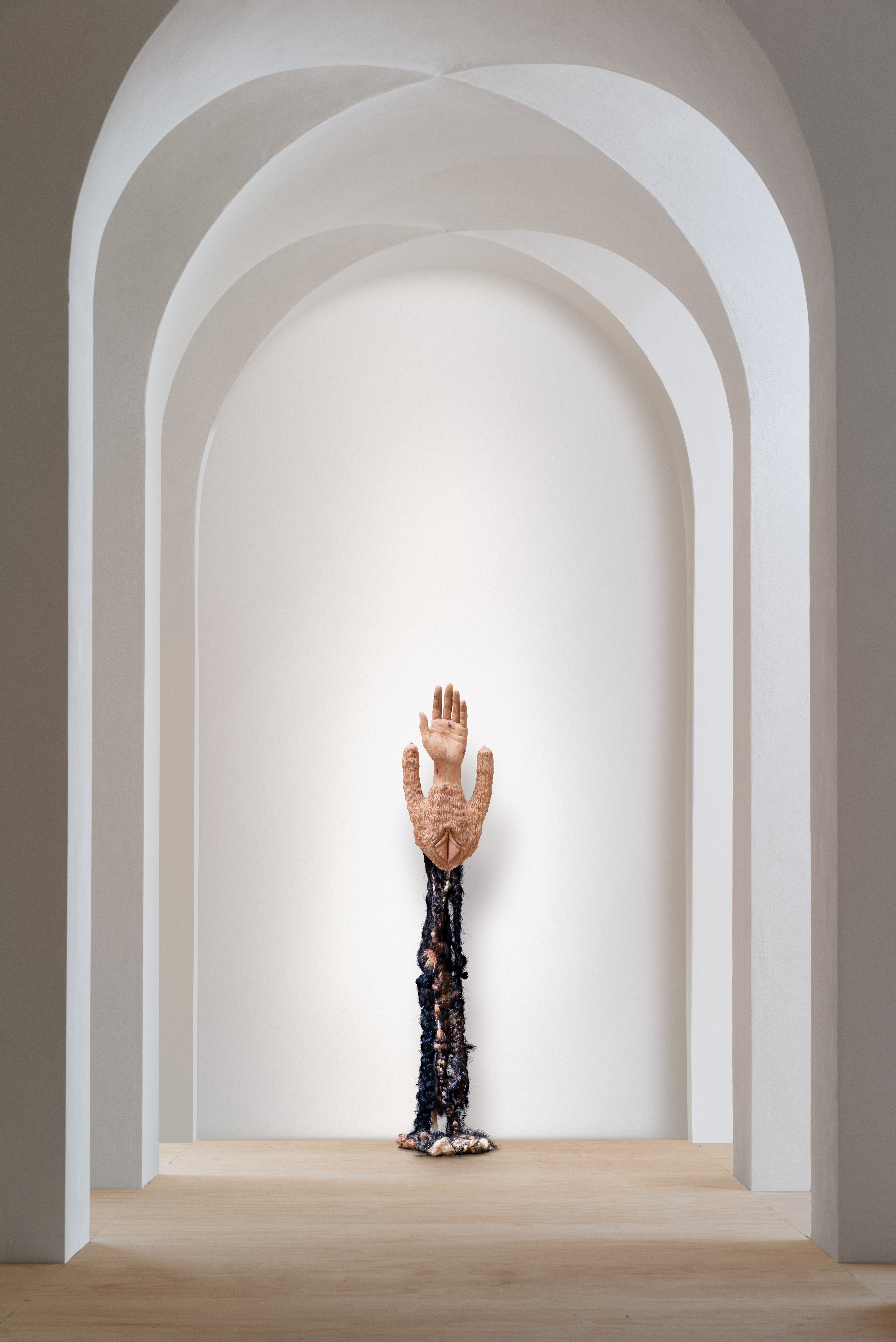 Een sculptuur van een lichaam op een sokkel van Femmy Otten uit de tentoonstelling Birthland, gecentreerd in een witte gewelfde gang van Museum Beelden aan Zee in Den Haag