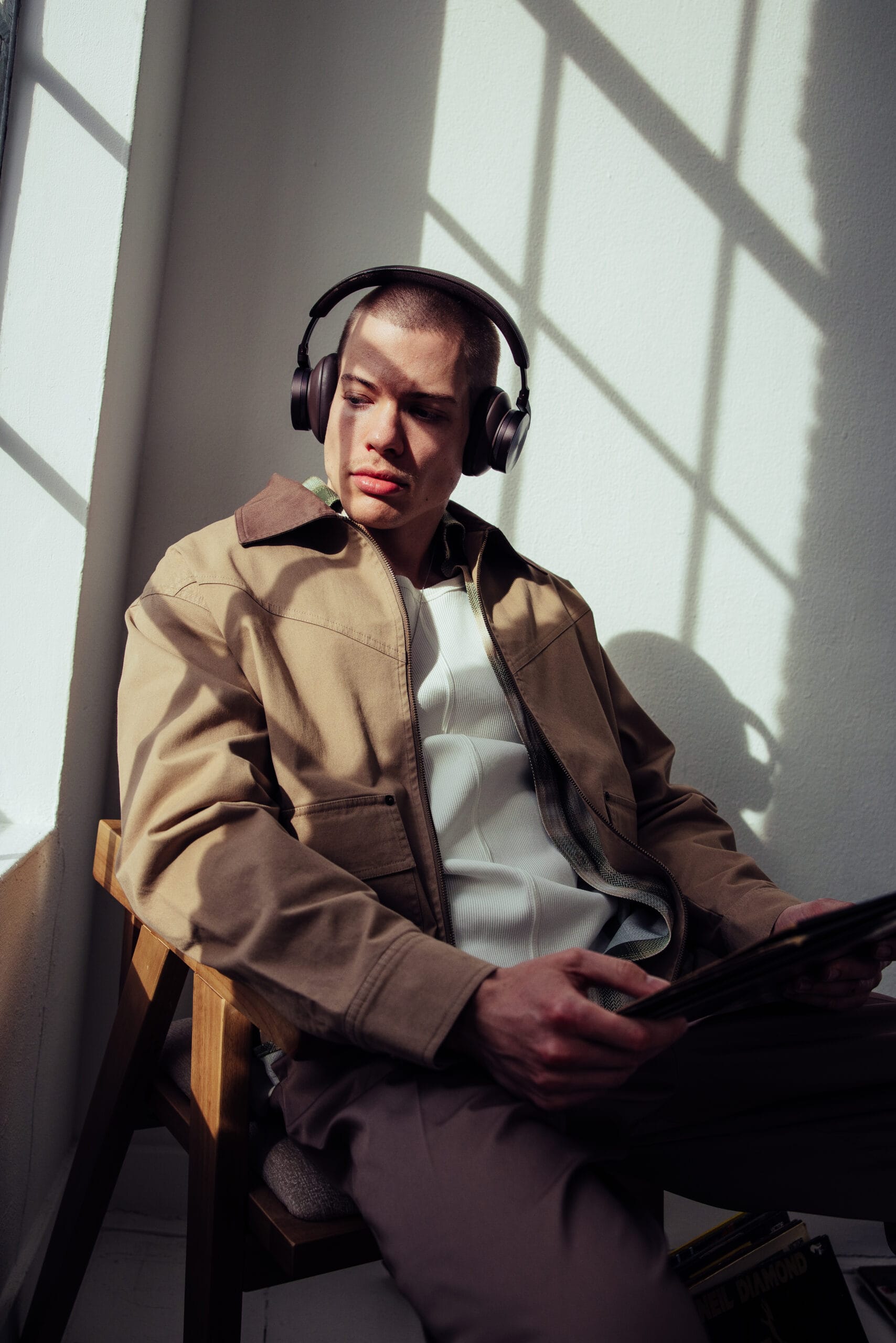 Een man met een koptelefoon op zit in een stoel bij een raam en bekijkt een lp-hoes
