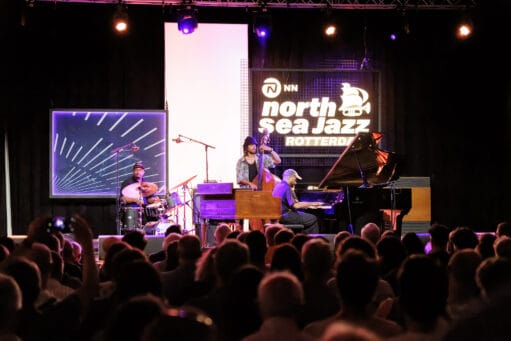 Een jazztrio met een drummer, contrabassist en pianist treedt op voor een zittend publiek bij North Sea Jazz Rotterdam