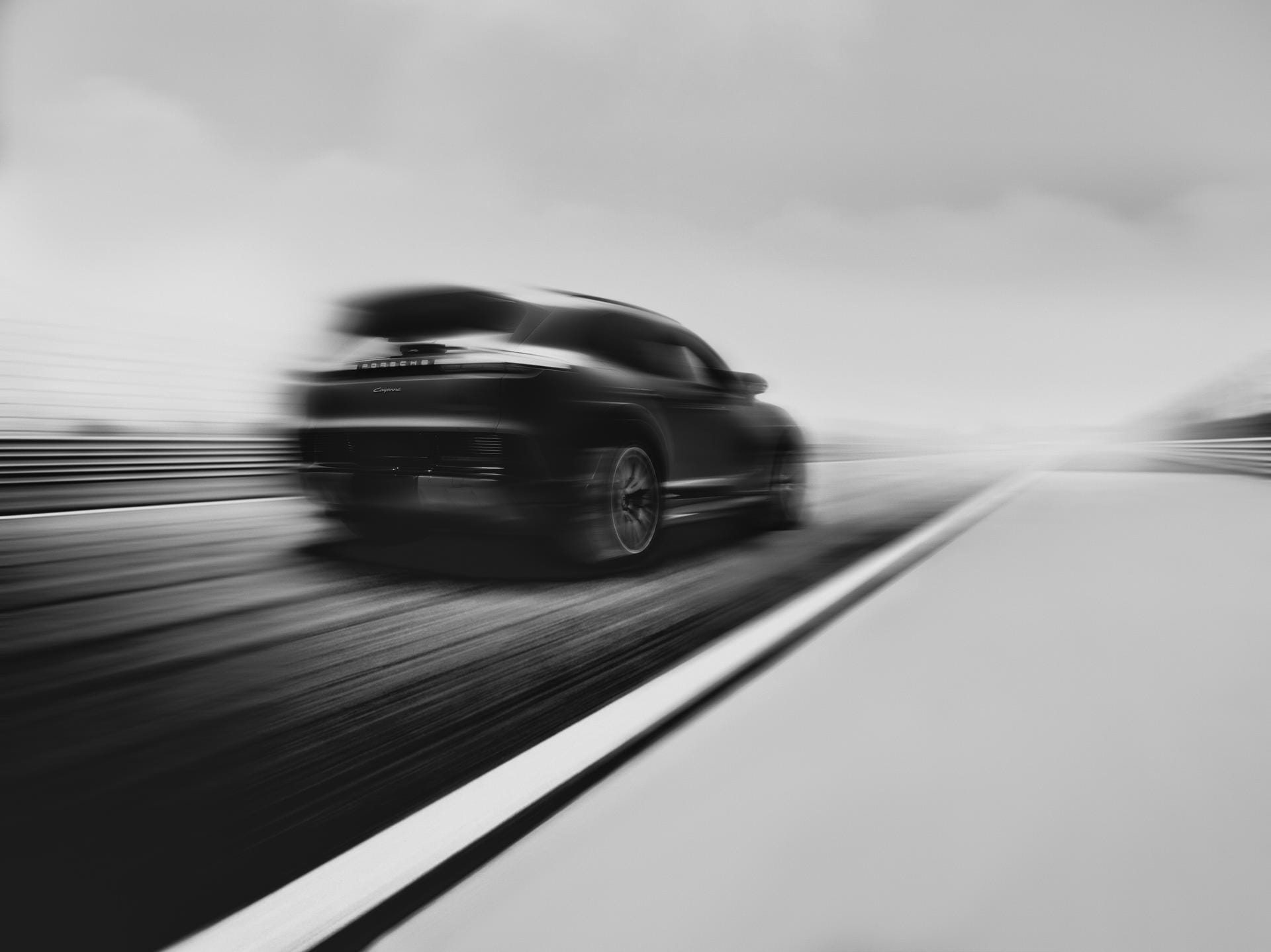 Een zwart-witfoto van een Porsche Cayenne die met hoge snelheid over een circuit rijdt met bewegingsonscherpte