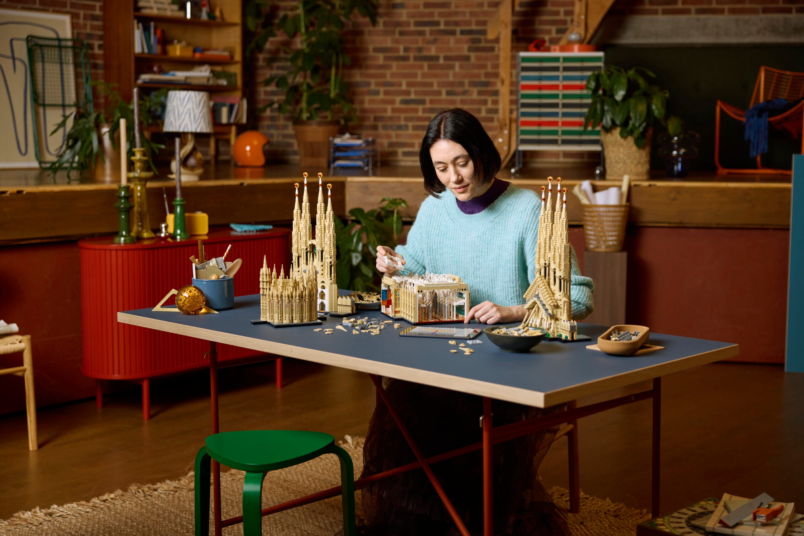 Een vrouw bouwt aan een gedetailleerd LEGO-model van de Sagrada Família aan een grote tafel in een atelier