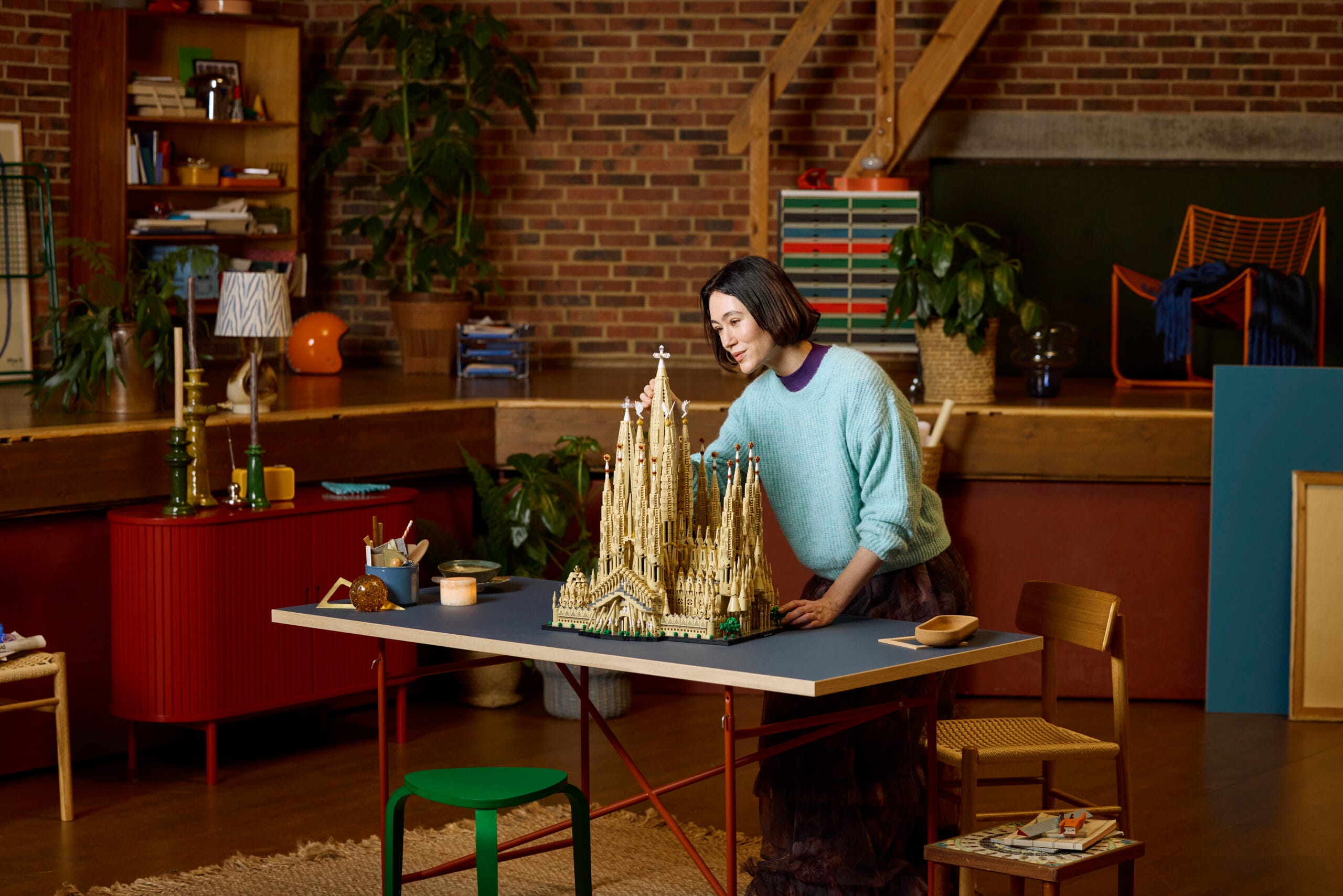 Een vrouw in een atelier plaatst de laatste hand aan een gedetailleerd LEGO model van de Sagrada Família op een tafel