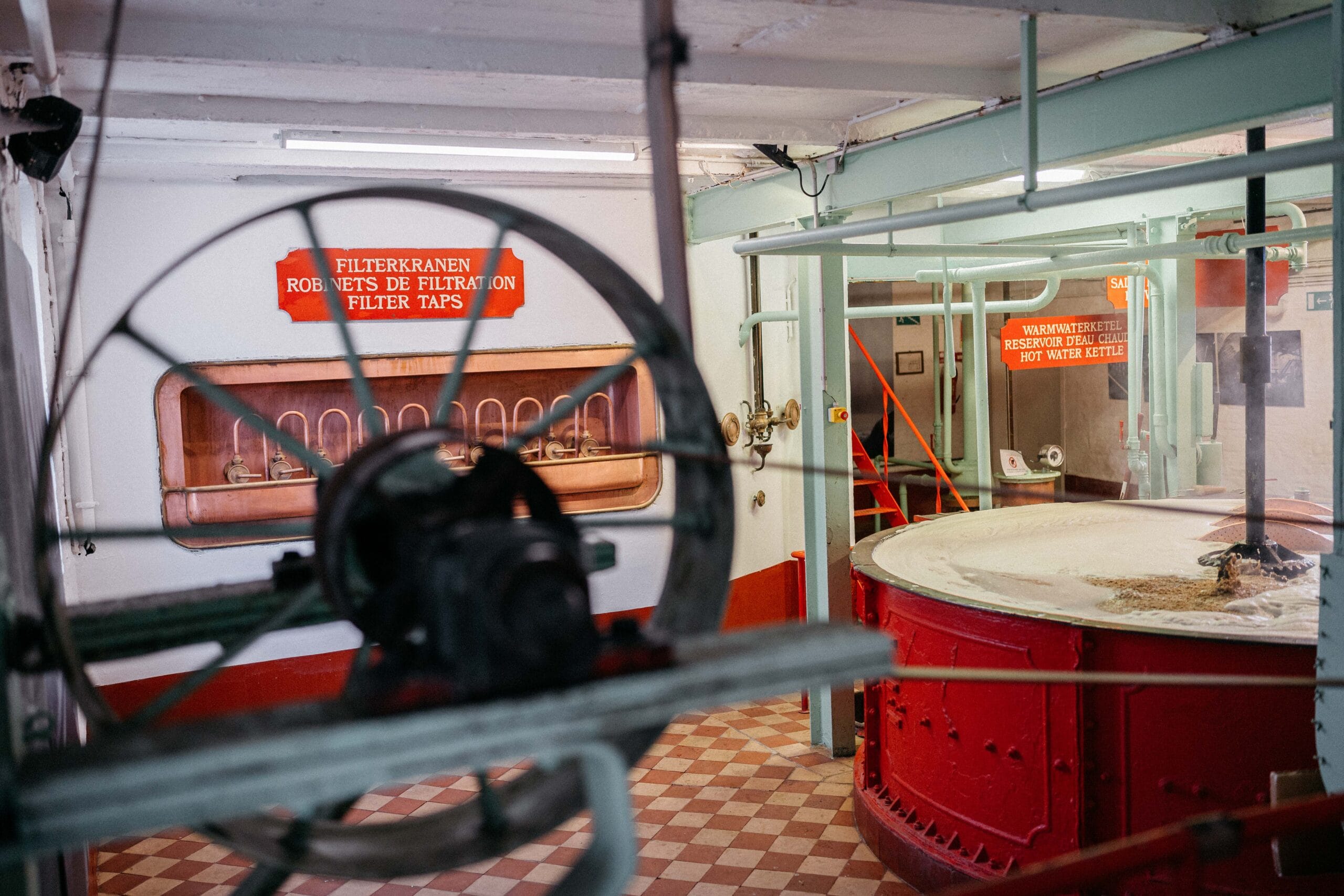 Interieur van een brouwerij met koperen filterkranen en een grote rode beslagkuip