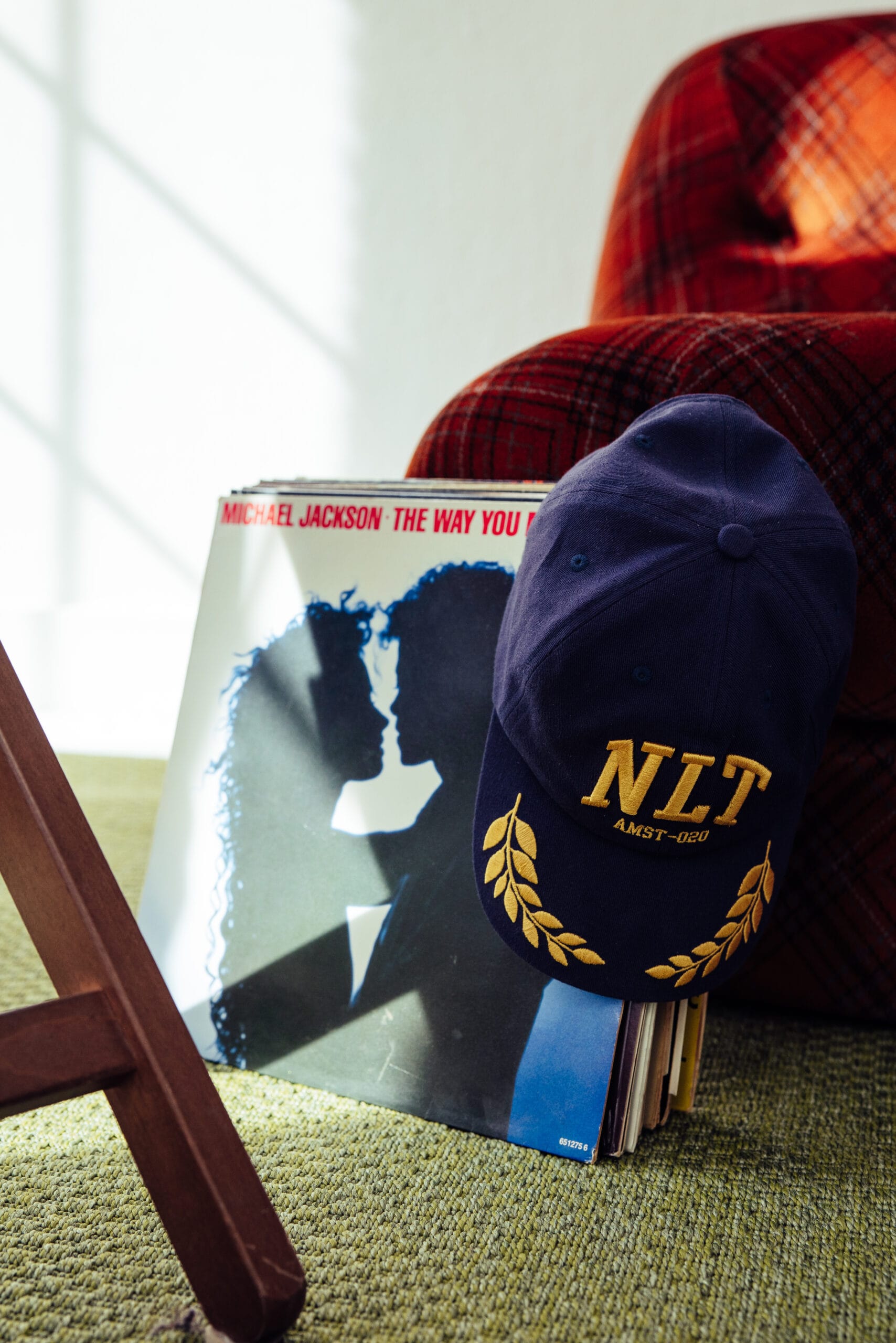 Een donkerblauwe pet met de letters NLT en goudkleurige lauwerkransen leunend tegen een stapel vinylplaten