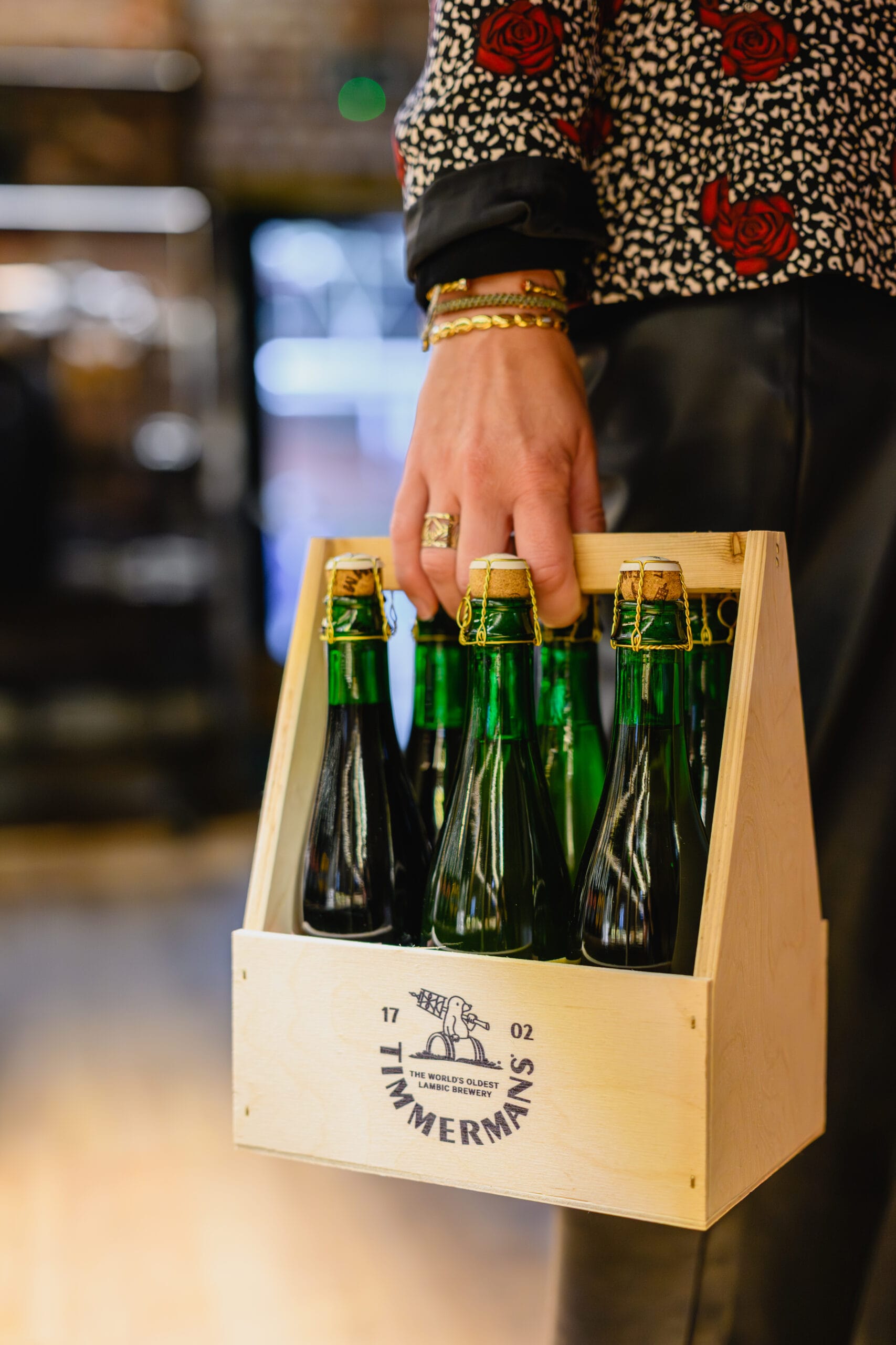 Een persoon draagt een houten kratje met flessen Timmermans lambiekbier