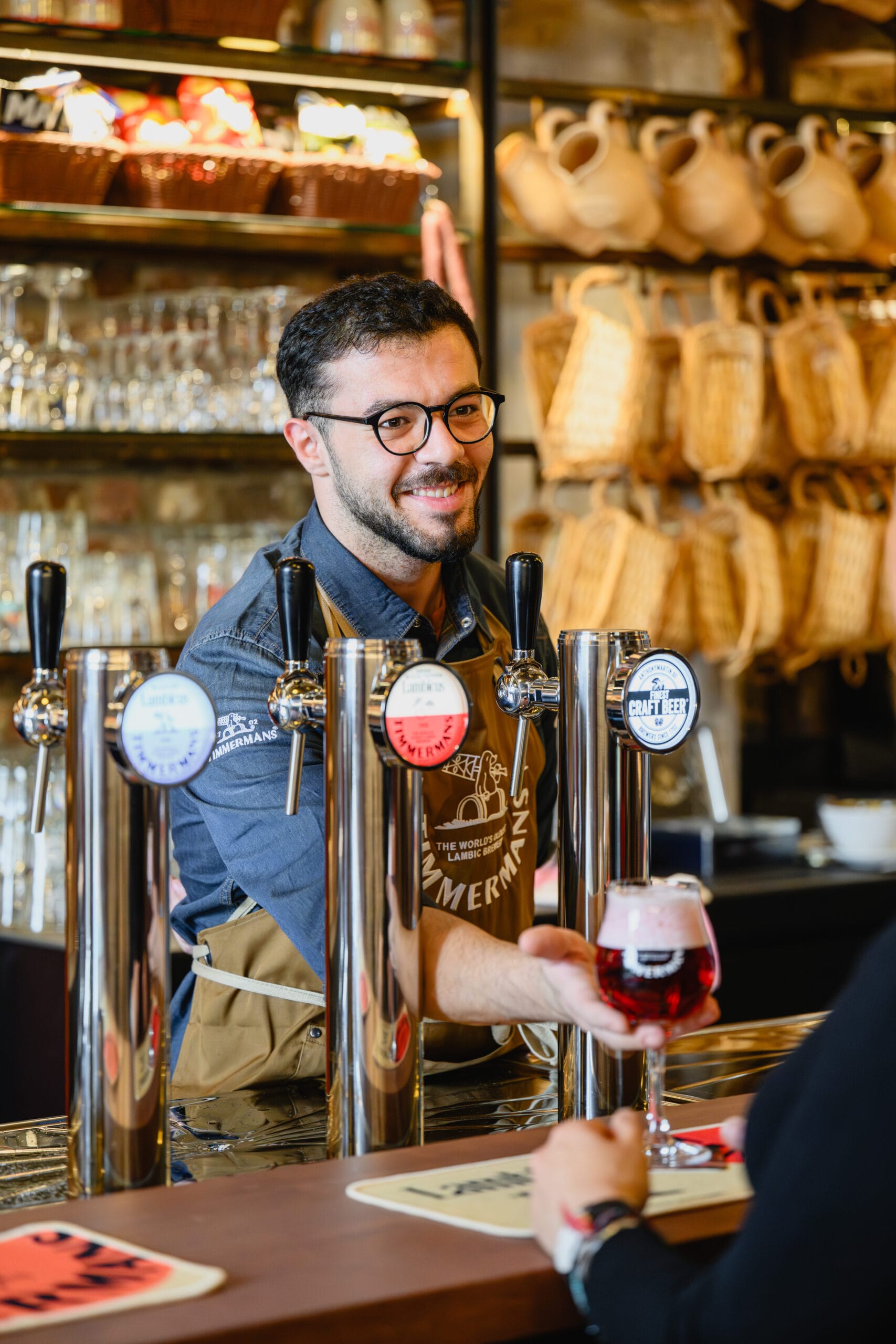 Een glimlachende barman serveert een glas rood speciaalbier aan een klant in een café