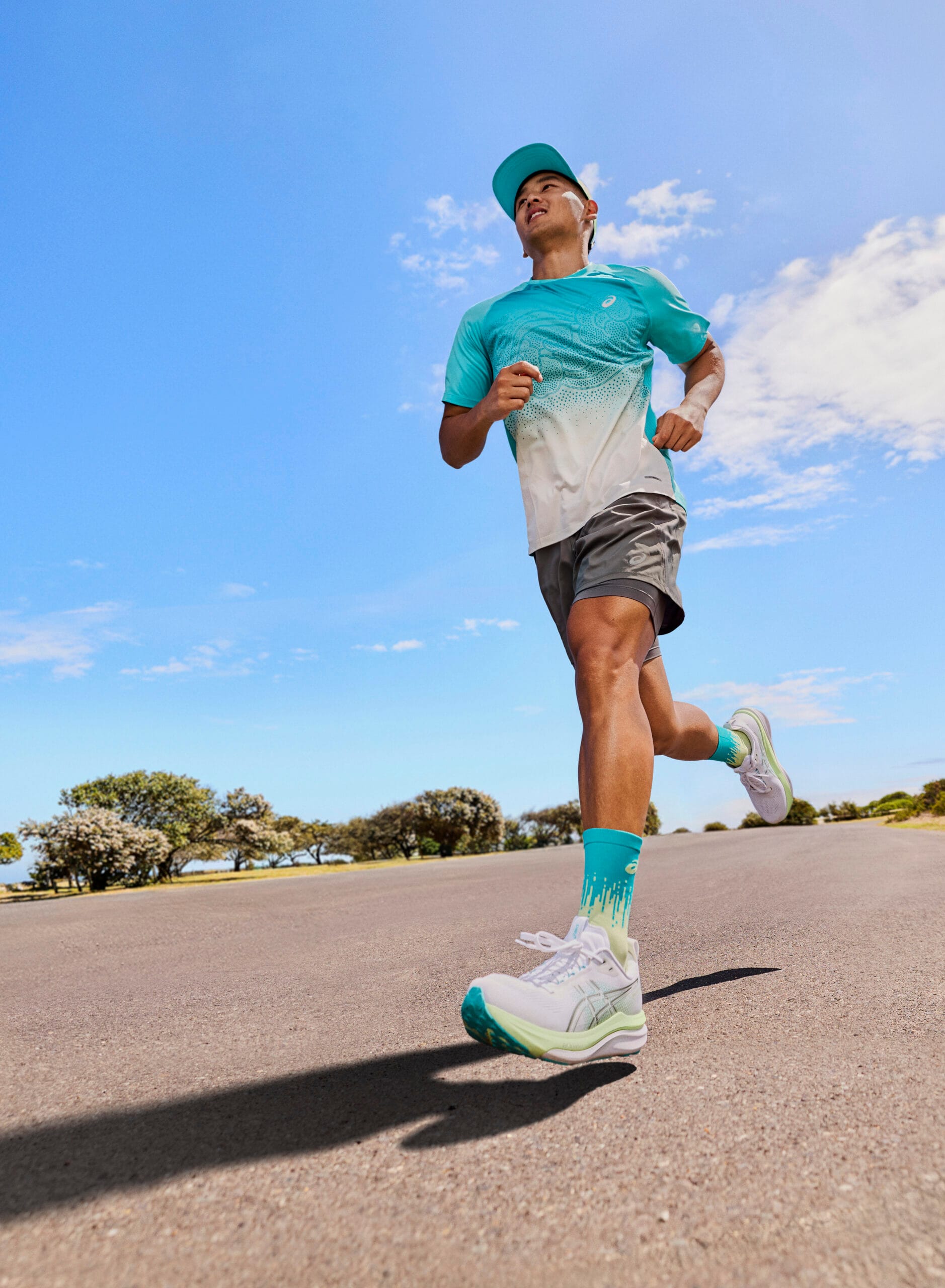 Hardloper in ASICS-sportkleding rent op de ASICS GEL-KAYANO 33 een zonnige weg tegen een blauwe lucht
