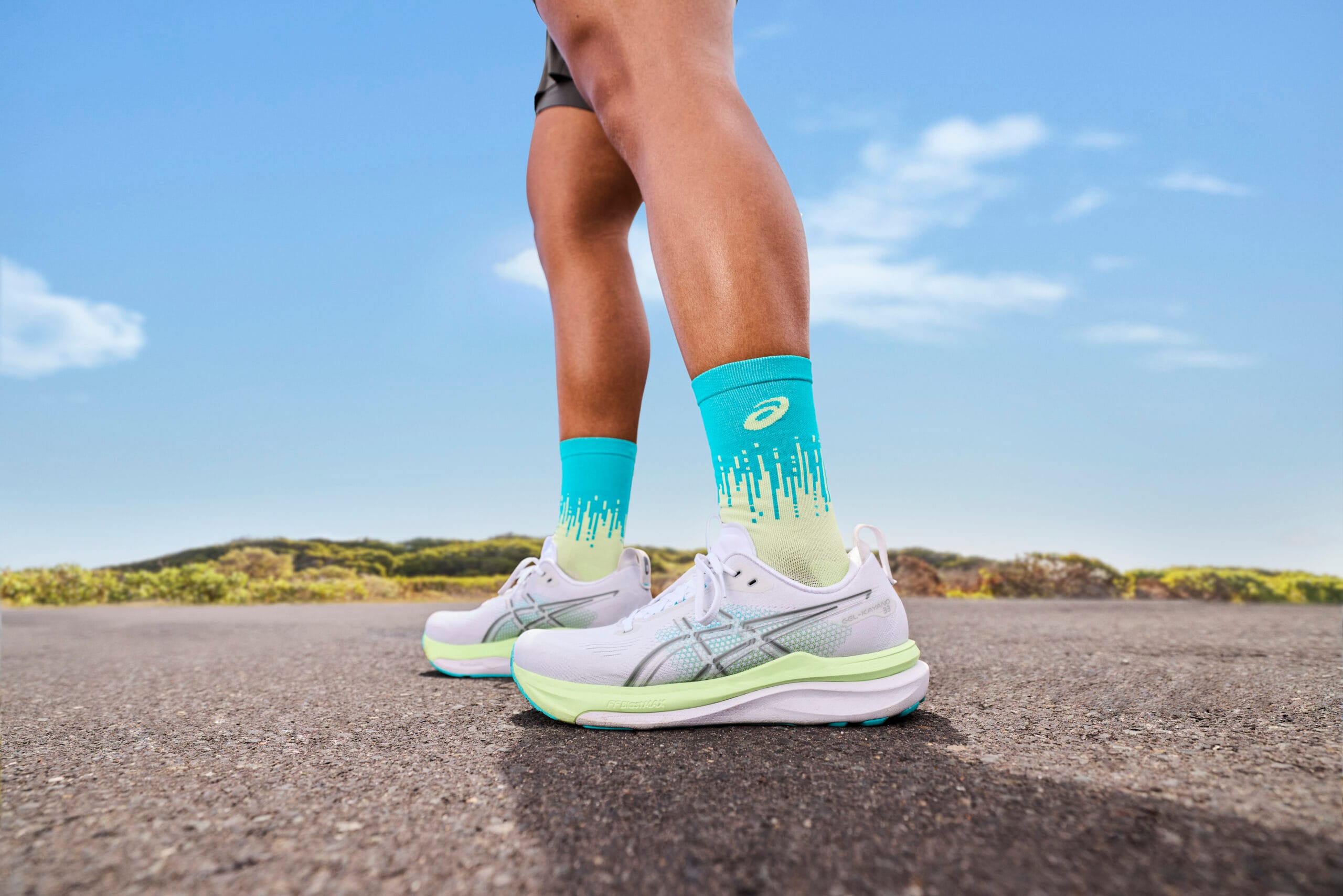 Hardloper op een weg met witte ASICS GEL-KAYANO 33 hardloopschoenen en opvallende blauw-gele sokken