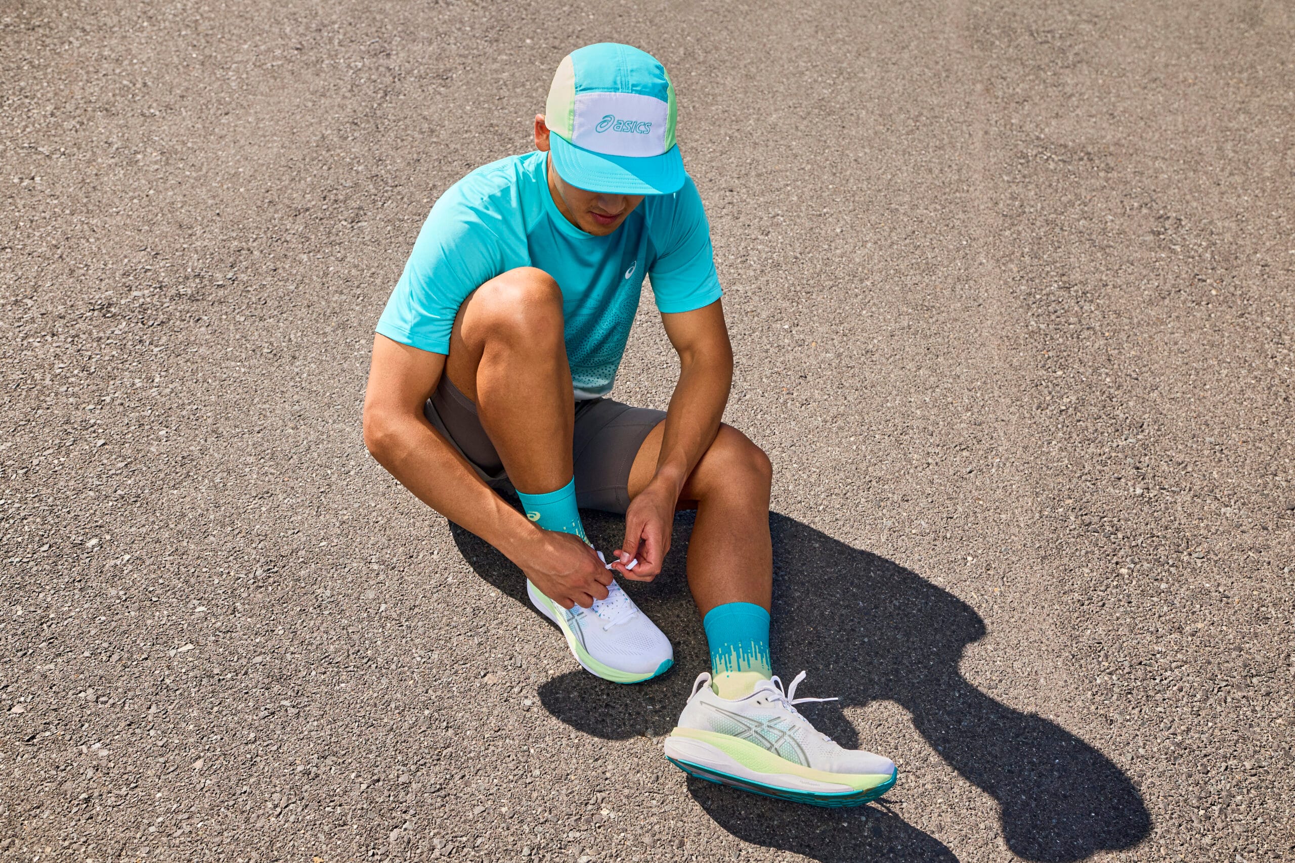 Hardloper zittend op het asfalt strikt de veters van zijn witte ASICS GEL-KAYANO 33 hardloopschoenen
