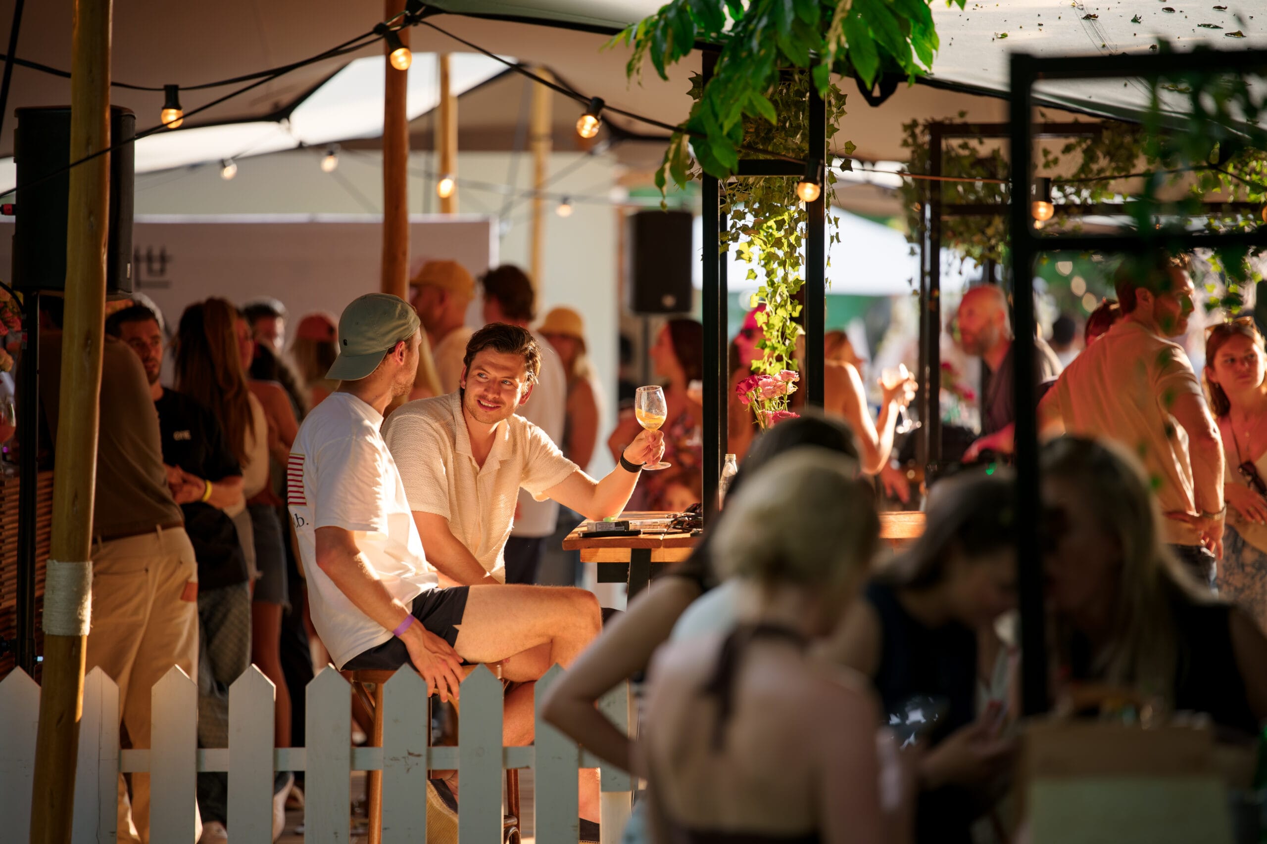 Twee mannen praten met elkaar aan een hoge tafel op een drukbezocht Bite of Amsterdam in de zon