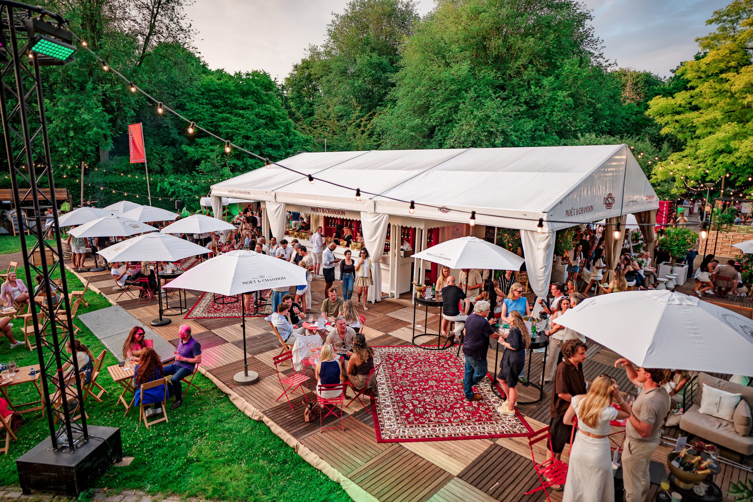 Gasten tijdens het zomerse buitenevenement Bite of Amsterdam bij een witte Moët & Chandon loungetent met parasols en houten vlonders