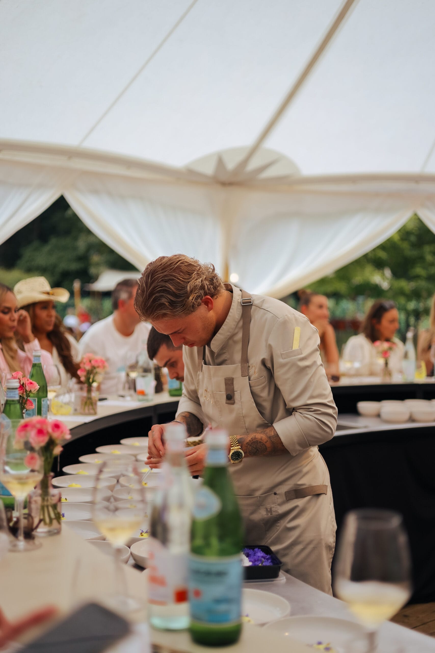 Een chef-kok in een beige schort maakt zorgvuldig borden op tijdens Bite of Amsterdam in een witte tent
