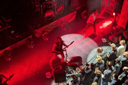 Metalband Blood Incantation treedt op een donker podium op met felrode belichting, terwijl fans vooraan bij het podium toekijken