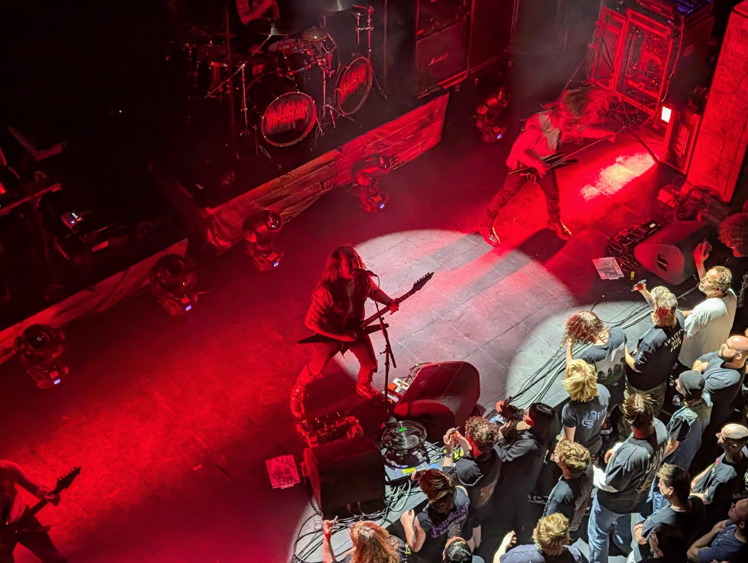 Metalband Blood Incantation treedt op een donker podium op met felrode belichting, terwijl fans vooraan bij het podium toekijken