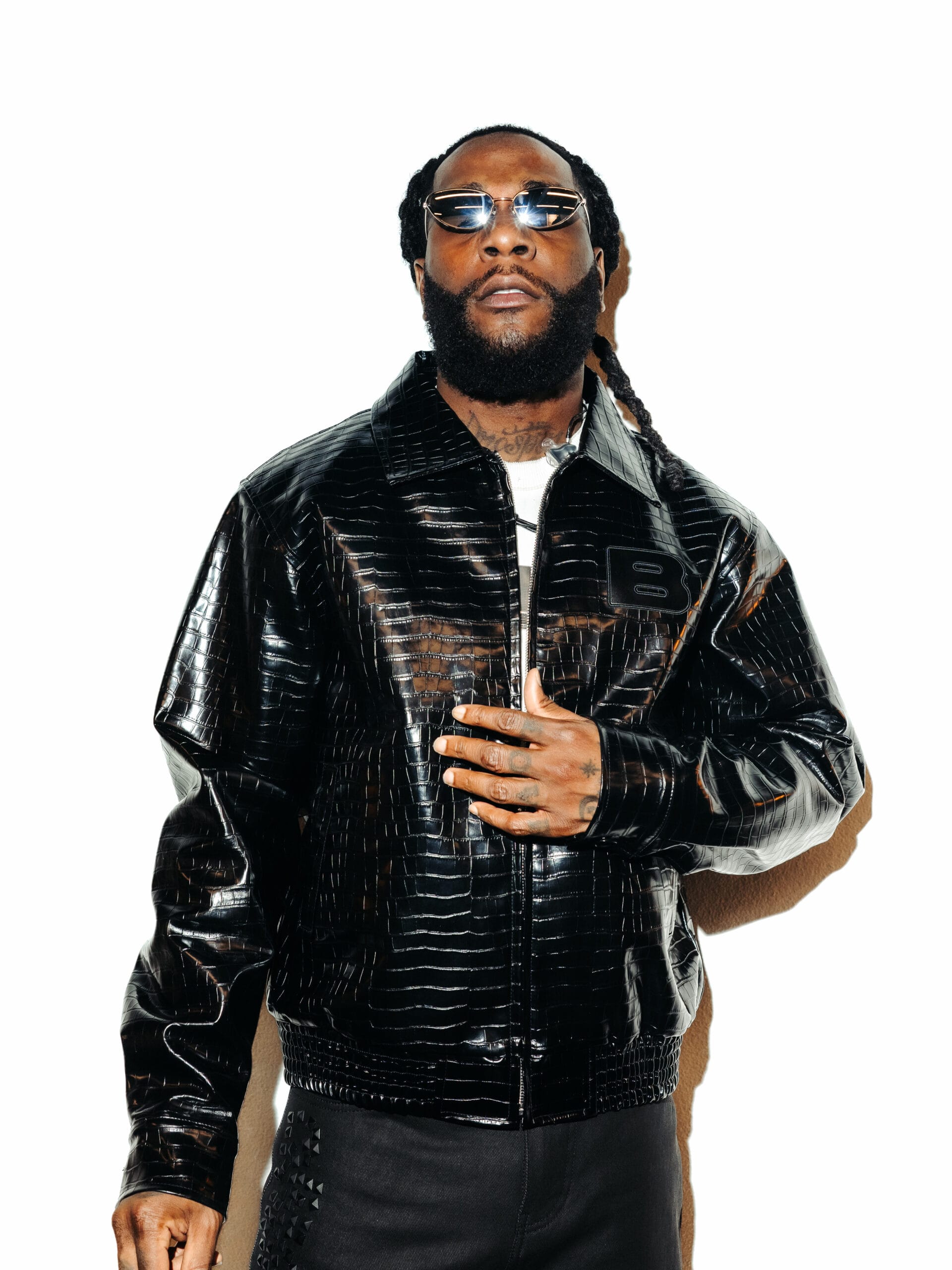 Portret van Burna Boy in een zwarte leren jas met krokodillenprint en een zonnebril tegen een witte achtergrond