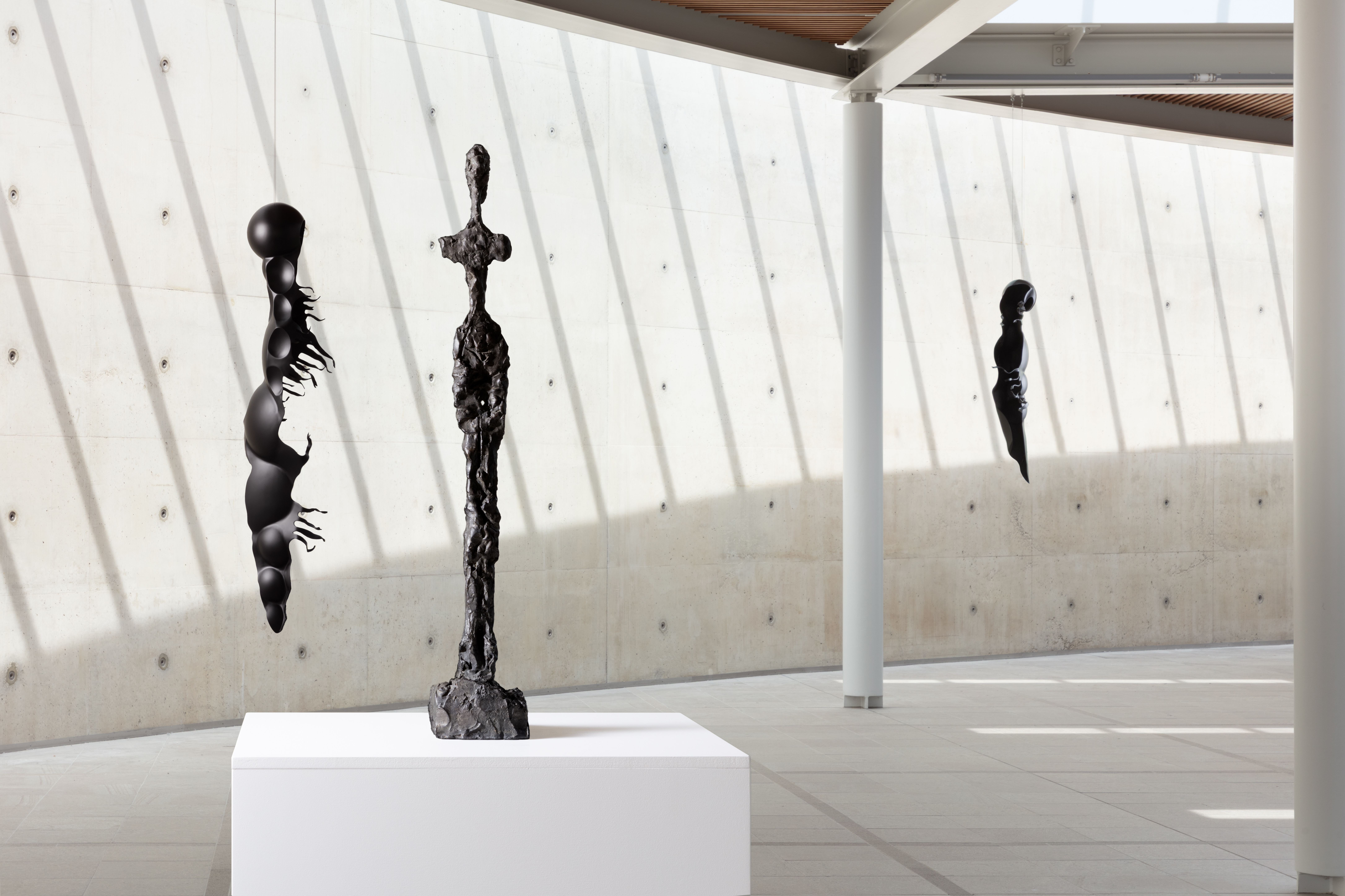 Drie abstracte zwarte sculpturen van de tentoonstelling Rui Chafes X Alberto Giacometti. Gris Vide Cris III in een lichte museumzaal van Beelden aan Zee met een betonnen muur en invallend zonlicht