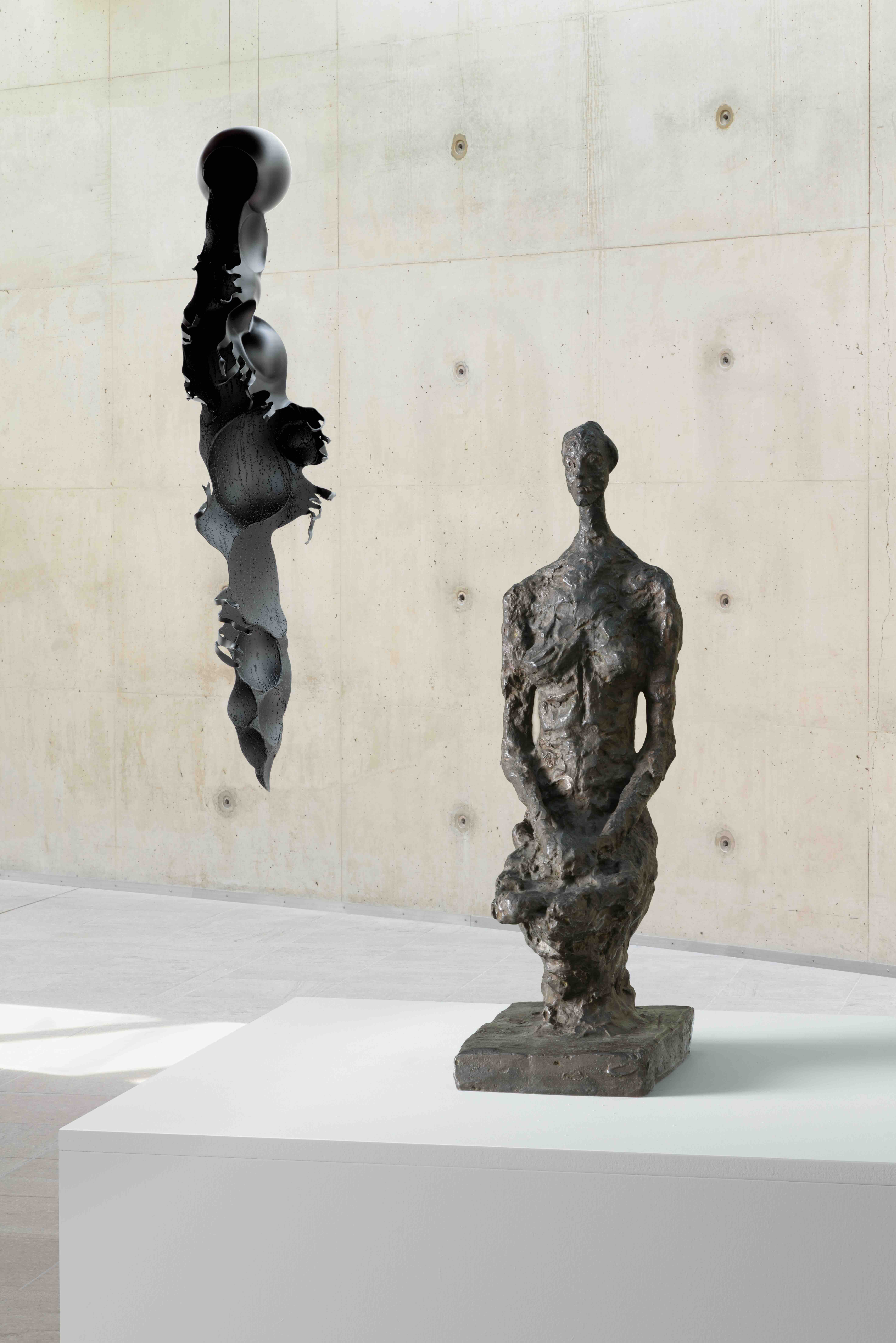 Een bronzen, ruw getextureerd menselijk figuur op een sokkel naast een abstracte, zwarte hangende sculptuur van de expositie Rui Chafes X Alberto Giacometti. Gris Vide Cris III in Museum Beelden aan Zee in Den Haag