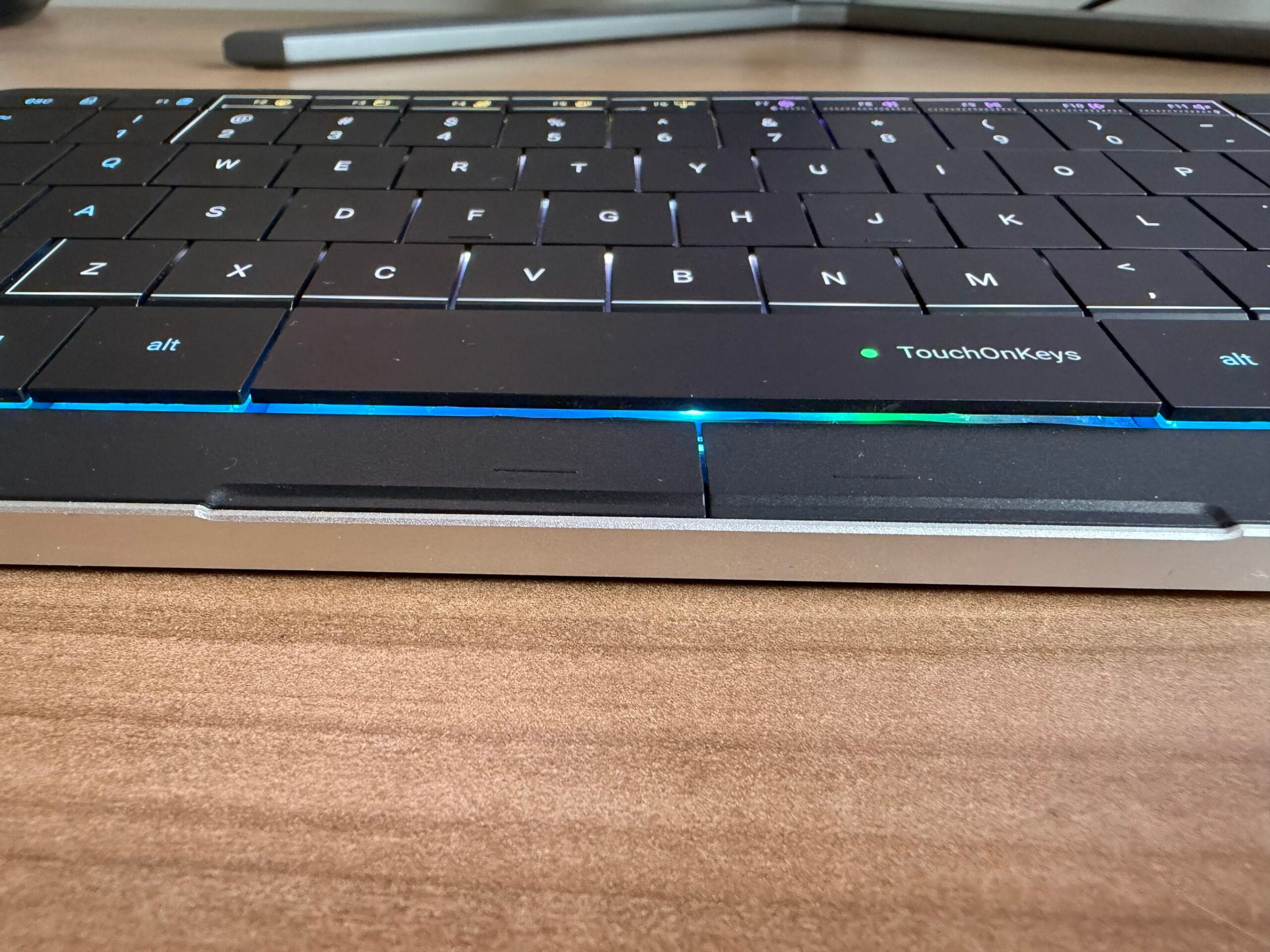 Zijaanzicht van een zwart TouchOnKeys-toetsenbord met verlichte toetsen en een blauwe lichtstrip aan de onderkant