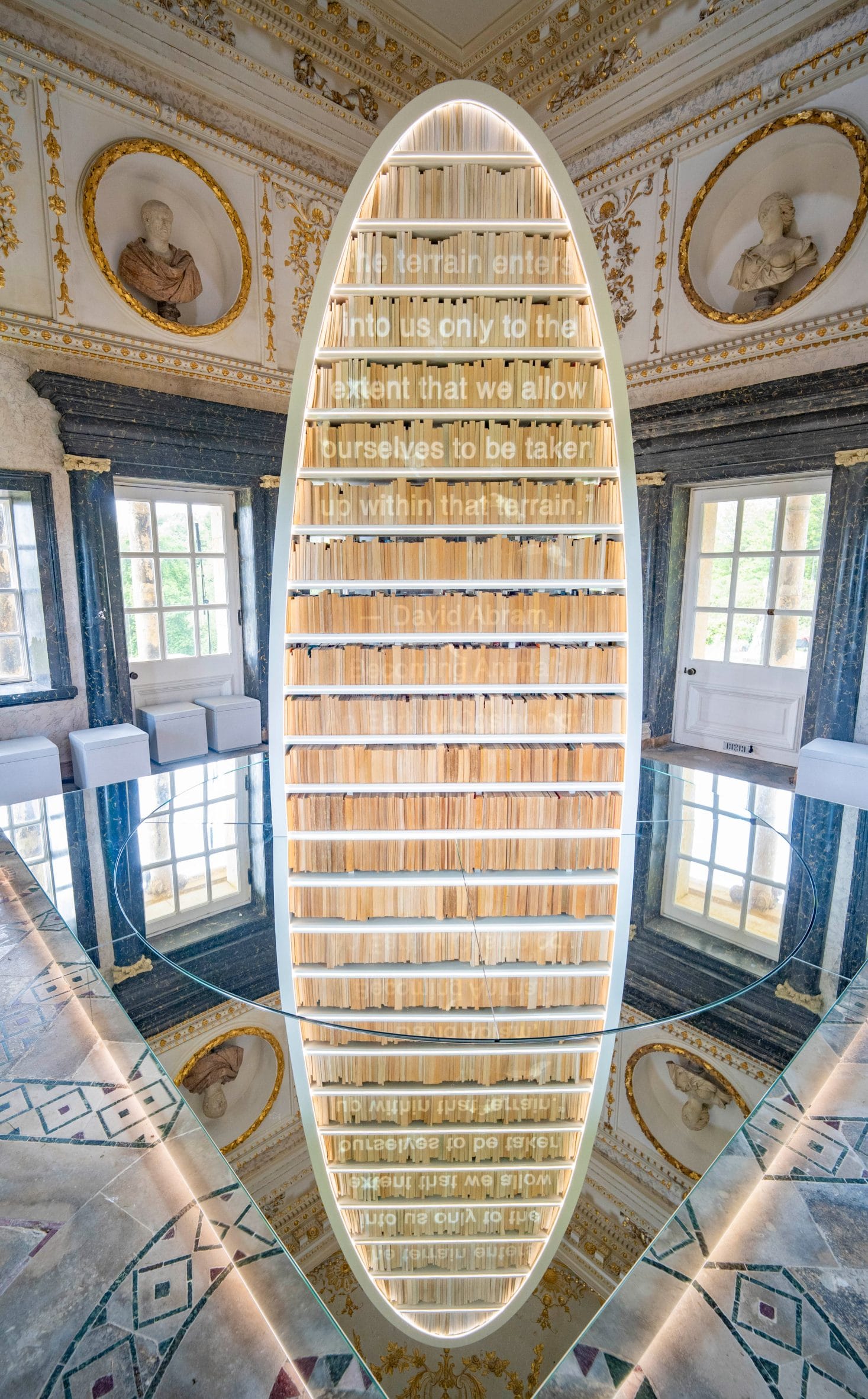 Een ovale boekenkast in een klassieke zaal met een citaat van David Abram op de glazen planken